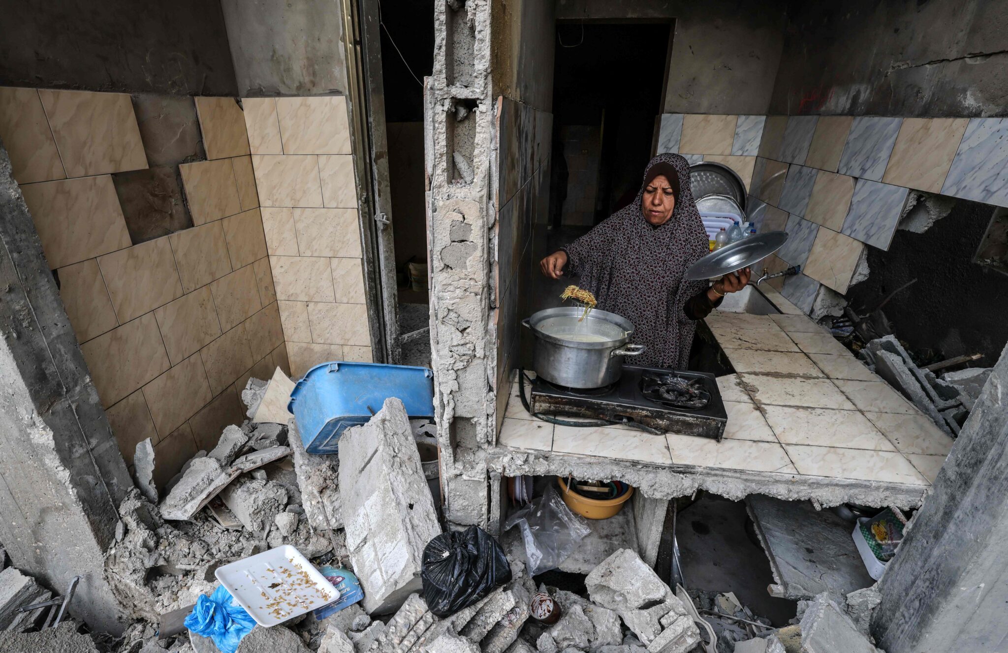 TOPSHOT - A Palestinian woman who has returned to her neighbourhood, cooks a meal in what remains of her home, hit by Israeli bombardment in Gaza City, after a ceasefire brokered by Egypt between Israel and Hamas, on May 21, 2021. A ceasefire between Israel and Hamas, the Islamist movement which controls the Gaza Strip, appeared to hold today after 11 days of deadly fighting that pounded the Palestinian enclave and forced countless Israelis to seek shelter from rockets. / AFP / MOHAMMED ABED