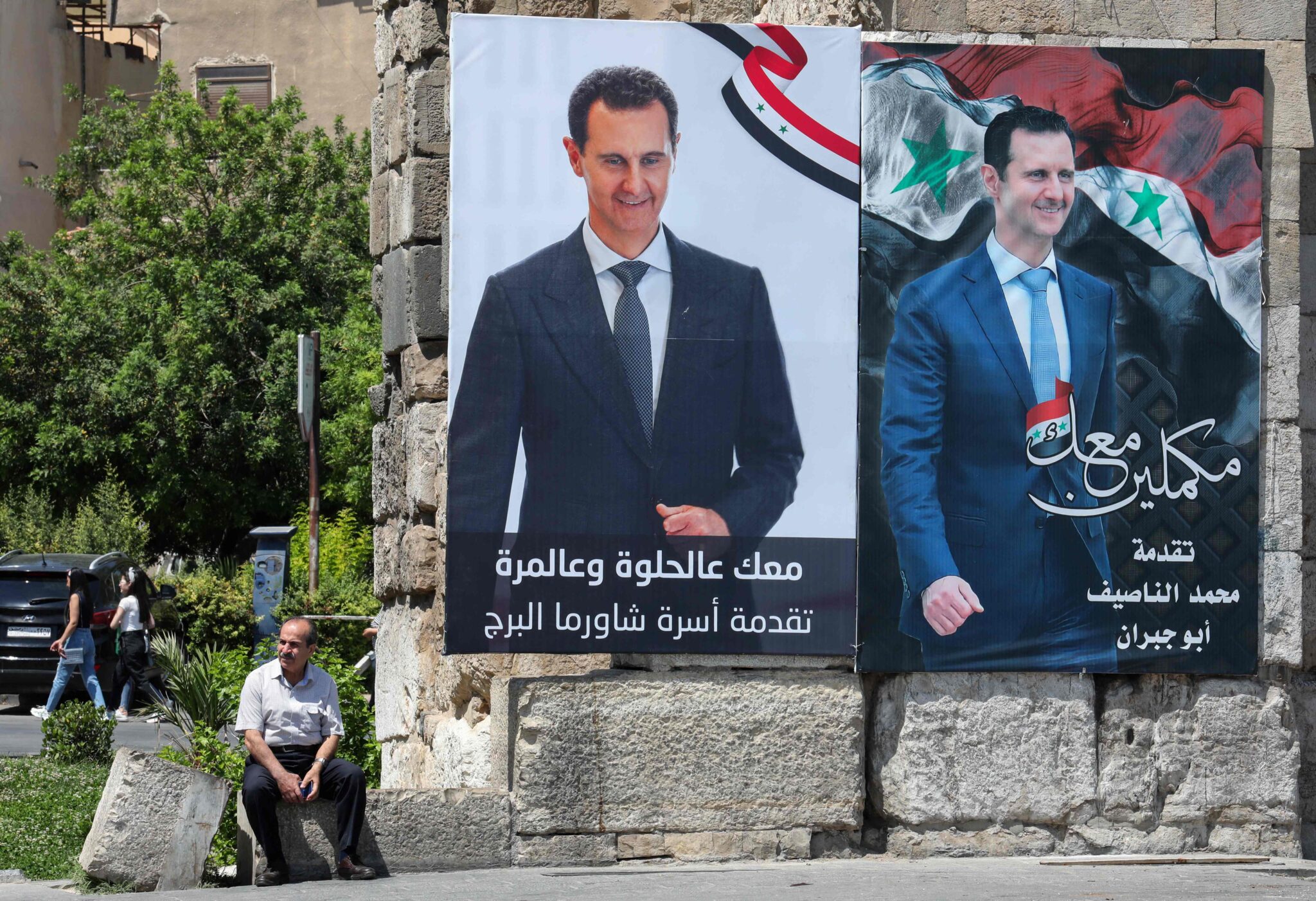 A man sits next to election campaign billboards depicting Syrian President Bashar al-Assad, a candidate for the upcoming presidential vote, in the capital Damascus on May 23, 2021. Al-Assad, whose family has ruled Syria for over half a century, faces an election this week meant to cement his image as the only hope for recovery in the war-battered country, analysts say. / AFP / LOUAI BESHARA