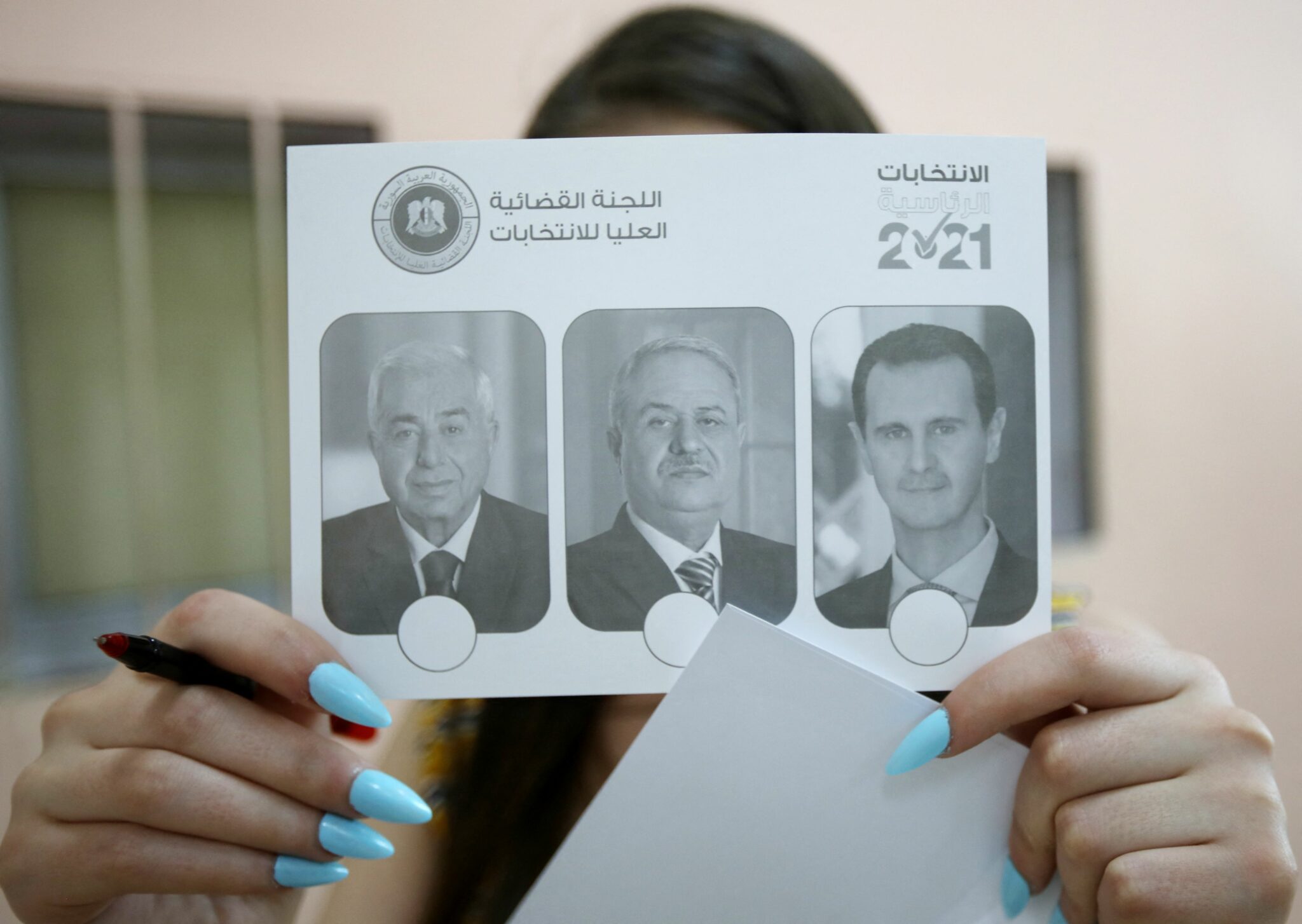 A Syrian voter, shows a ballot with the pictures of the three candidates in Syria's presidential election, including President Bashar al-Assad (), before casting her vote at a polling station in Damascus on May 26, 2021. The 55-year-old Assad, who has been in power since 2000, is sure to keep his job after the election, every aspect of which is controlled by him and his Baath party. He faces former state minister Abdallah Salloum Abdallah and Mahmoud Merhi, a member of the so-called "tolerated opposition", long described by exiled opposition leaders as an extension of the regime. / AFP / Louai Beshara