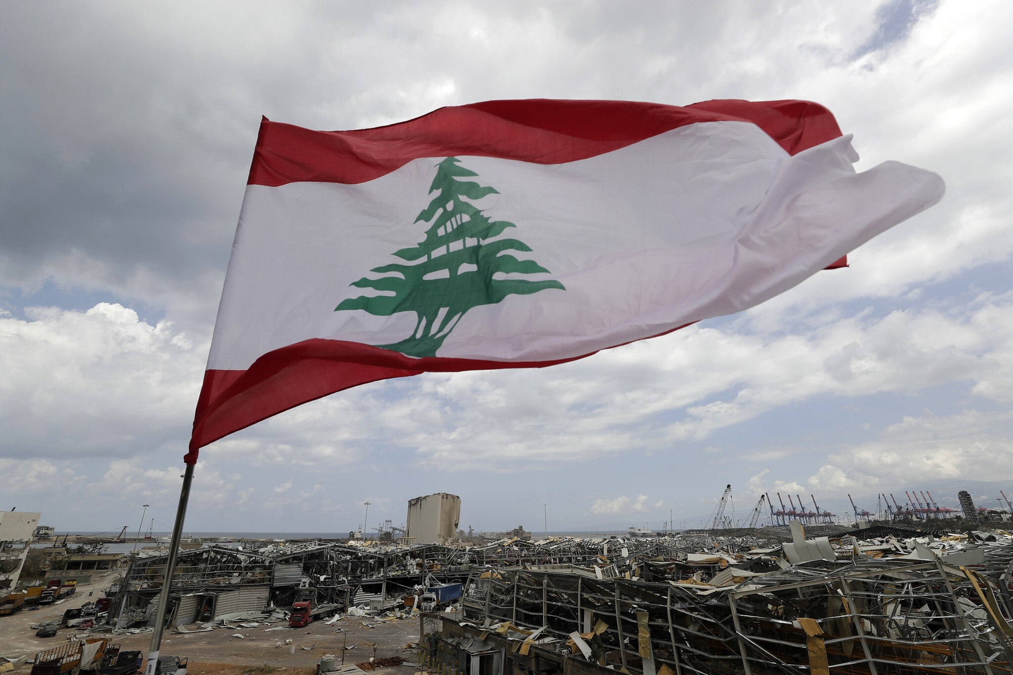 A Lebanese flag set by citizens flies in front the site of Tuesday's explosion that hit the seaport of Beirut, Lebanon, Sunday, Aug. 9, 2020. Lebanon's information minister resigned on Sunday as the country grapples with the aftermath of the devastating blast that ripped through the capital and raised public anger to new levels. (AP Photo/Hassan Ammar)