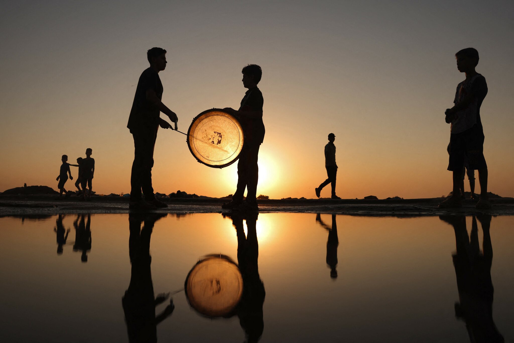 Palestinian children bang a drum near a beach at sunset in Gaza City on August 3, 2021. (Photo by MOHAMMED ABED / AFP)