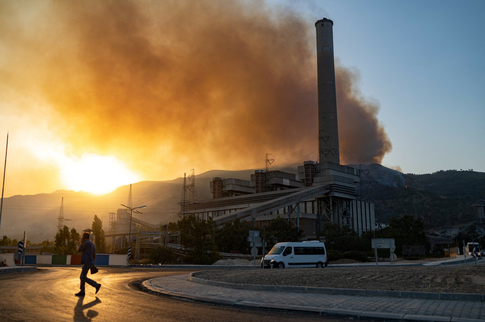 TOPSHOT - A man walk crosses a road in the vicinity of a forest fire close to the Kemerkoy Thermal Power Plant, at Oren in Milas, northen Turkey on August 4, 2021. A Turkish thermal power plant on the Aegean Sea was being evacuated on August 4, as a wildfire that has raged across the country for the past week reached its edge.Rescuers used helicopters and water cannon, in a fitful fight to save a Turkish power plant from being engulfed by deadly wildfires testing the leadership of President Recep Tayyip Erdogan. (Photo by Yasin AKGUL / AFP)