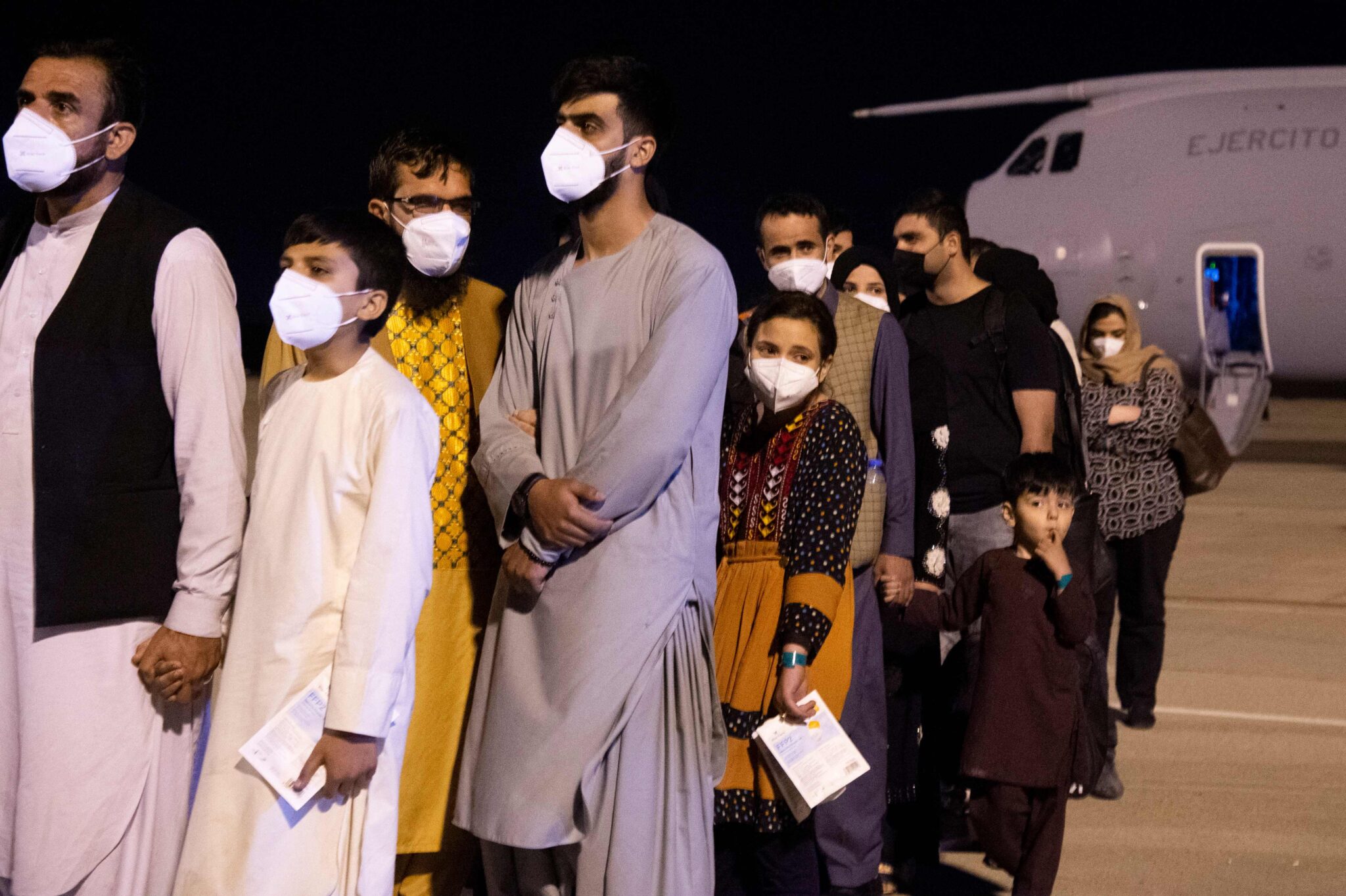 A group of Afghan nationals wait on the tarmac after disembarking from a first Spanish Air Force Airbus A400M that carrying Spaniards who still remained in Afghanistan as well as the Afghans and their families who collaborated with Spain, that landed at the Torrejon de Ardoz air base, 30 km away from Madrid, early on August 19, 2021. Afghans and foreigners have been desperately trying to flee the country since the Taliban's comeback, with the United States and other nations stepping up evacuation airlifts from Kabul. (Photo by Belen Diaz / AFP)