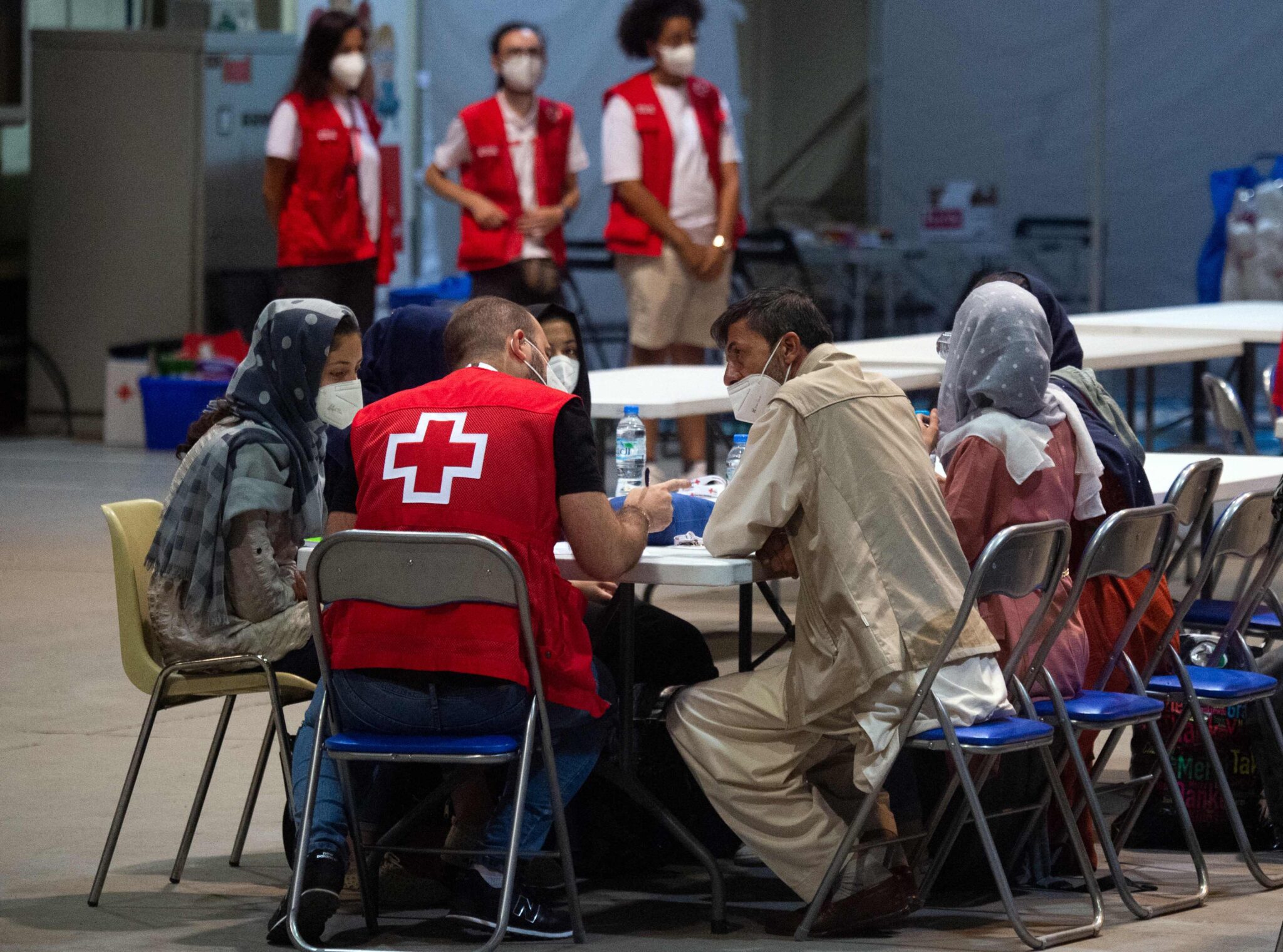 Red Cross volunteers talk with Afghan nationals upon their arrival onboard a first Spanish Air Force Airbus A400M carrying "just over 50 people" on board, including Spaniards who still remained in Afghanistan as well as the Afghans and their families who collaborated with Spain, at the Torrejon de Ardoz air base, 30 km away from Madrid, early on August 19, 2021. Afghans and foreigners have been desperately trying to flee the country since the Taliban's comeback, with the United States and other nations stepping up evacuation airlifts from Kabul. (Photo by Belen Diaz / AFP)