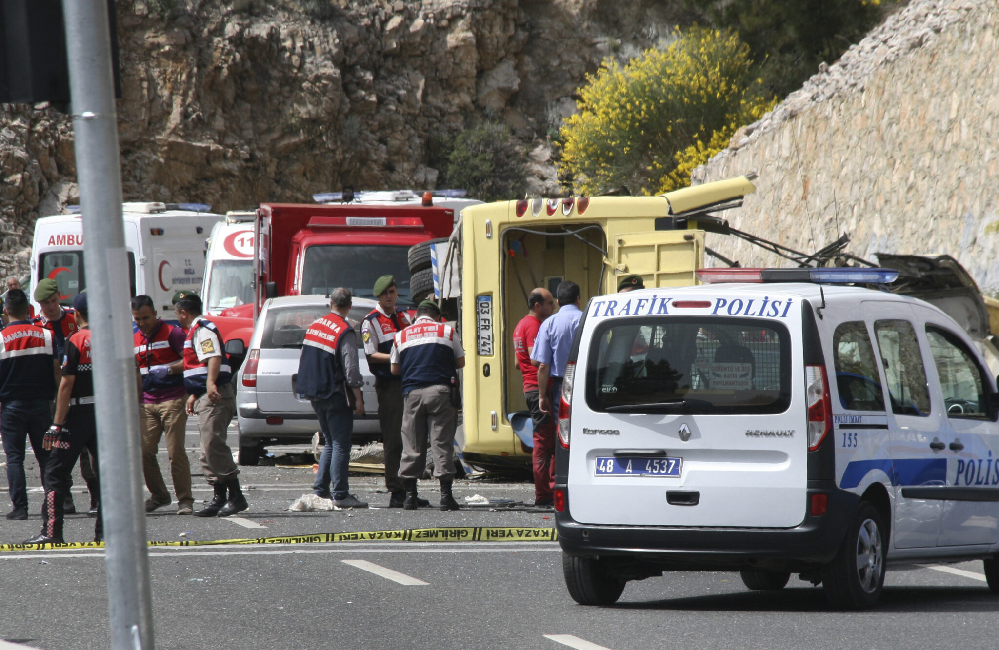 Turkish police officers work next to an overturned bus at the scene of a traffic accident, near Marmaris, western Turkey, Saturday, May 13, 2017. Turkish authorities say that over 20 people have died and nearly a dozen injured are in critical condition after a tour bus tipped over, fell 15 meters (50 feet) down a cliff and then hit a car on a serpentine mountain road. (IHA via AP)