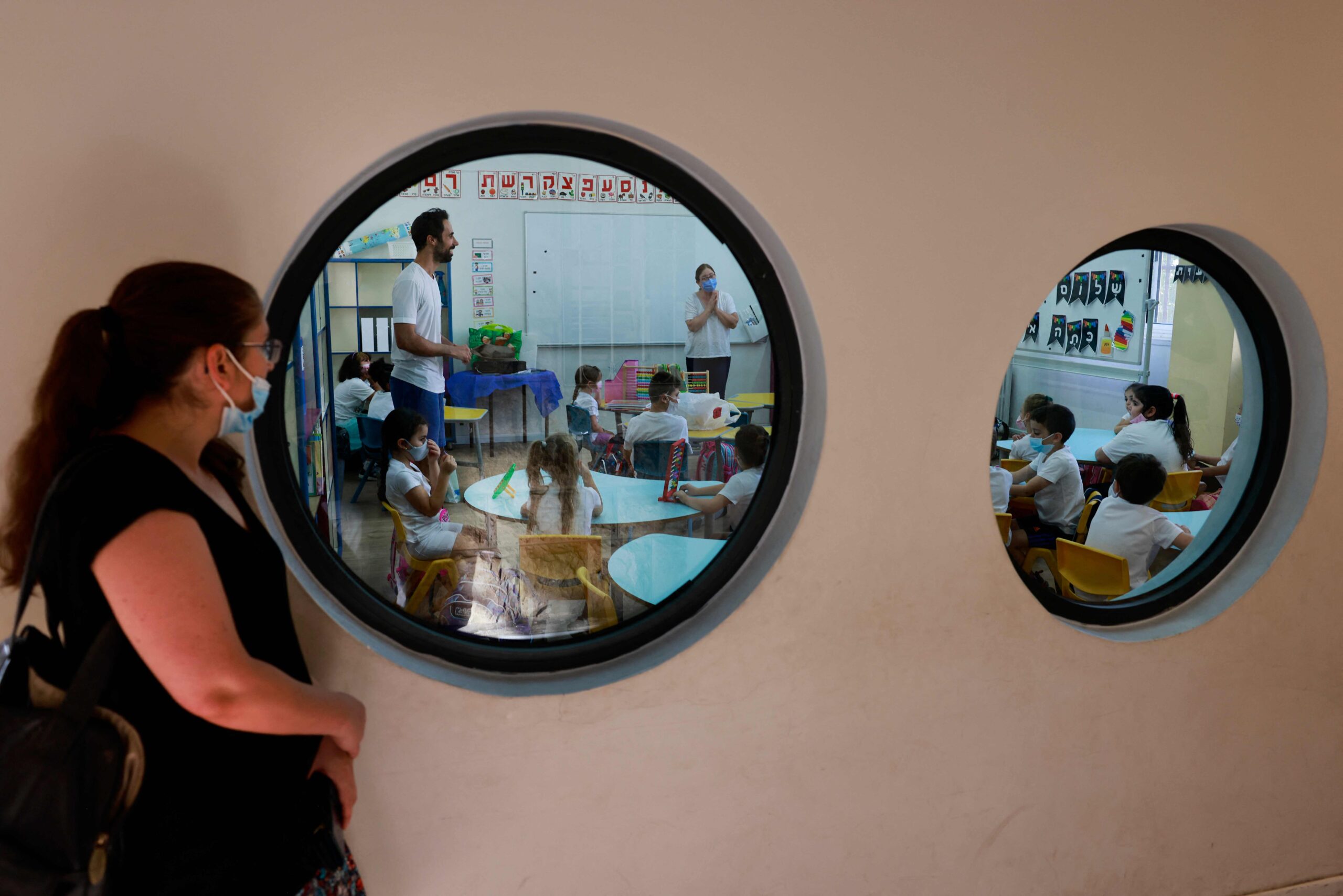 A woman looks at pupils wearing protective face maks upon their return to the new school year amid a surge of Covid-19 cases in Israel, at Beit Hakerem Israeli elementary school in Jerusalem, on September 1, 2021. Israel, which registered 7,000 new cases on August 29, this week passed the one million cases threshold since the pandemic began. The latest surge has largely been blamed on the highly transmissible Delta variant. More than 6,950 people have died from the virus in Israel. (Photo by MENAHEM KAHANA / AFP)