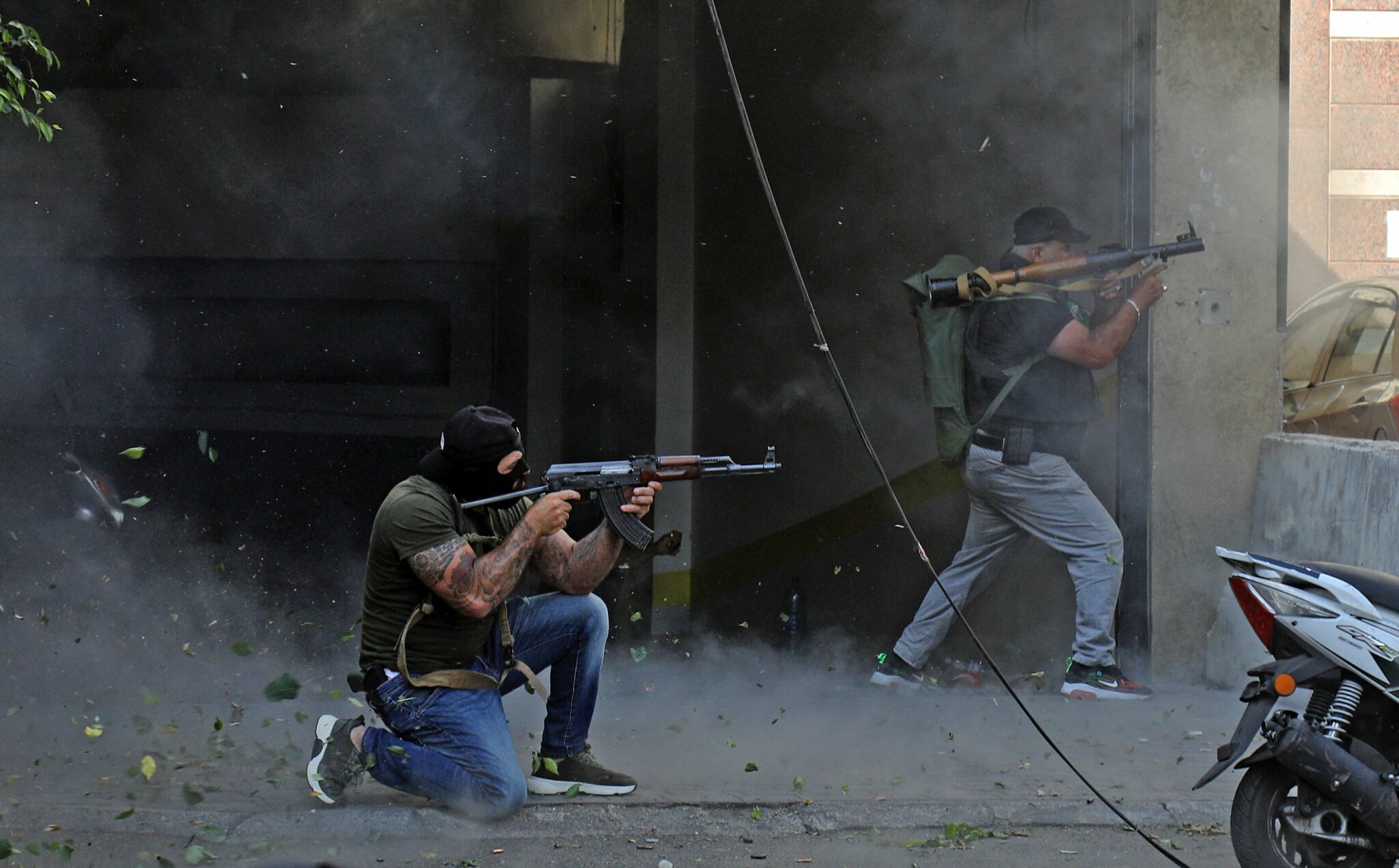 Shiite fighters from Hezbollah and Amal movements take aim with (L to R) a Kalashnikov assault rifle and a rocket-propelled grenade launcher amidst clashes in the area of Tayouneh, in the southern suburb of the capital Beirut, on October 14, 2021. Gunfire killed several people and wounded 20 at a Beirut rally organised by the Shiite Hezbollah and Amal movements to demand the dismissal of the Beirut blast lead investigator, the state-run National News Agency said. (Photo by IBRAHIM AMRO / AFP)