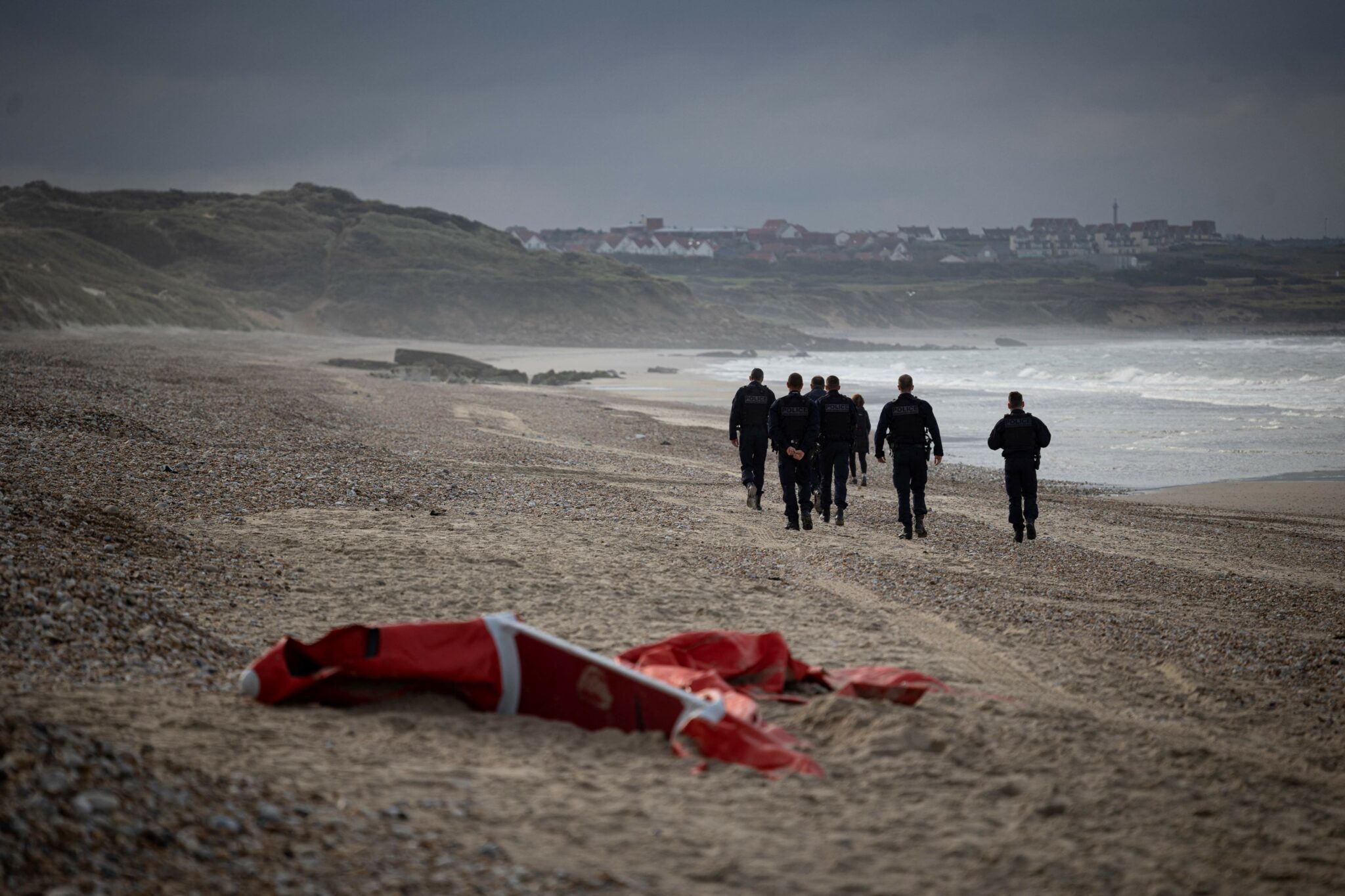 CORRECTION / TOPSHOT - French police officers patrolling the beach between Ambleteusse and Wimereux, northern France, pass by the wreckage of a inflatable boat used by migrants who attempt to cross the Channel towards England, on October 16, 2021. (Photo by Marc SANYE / AFP)