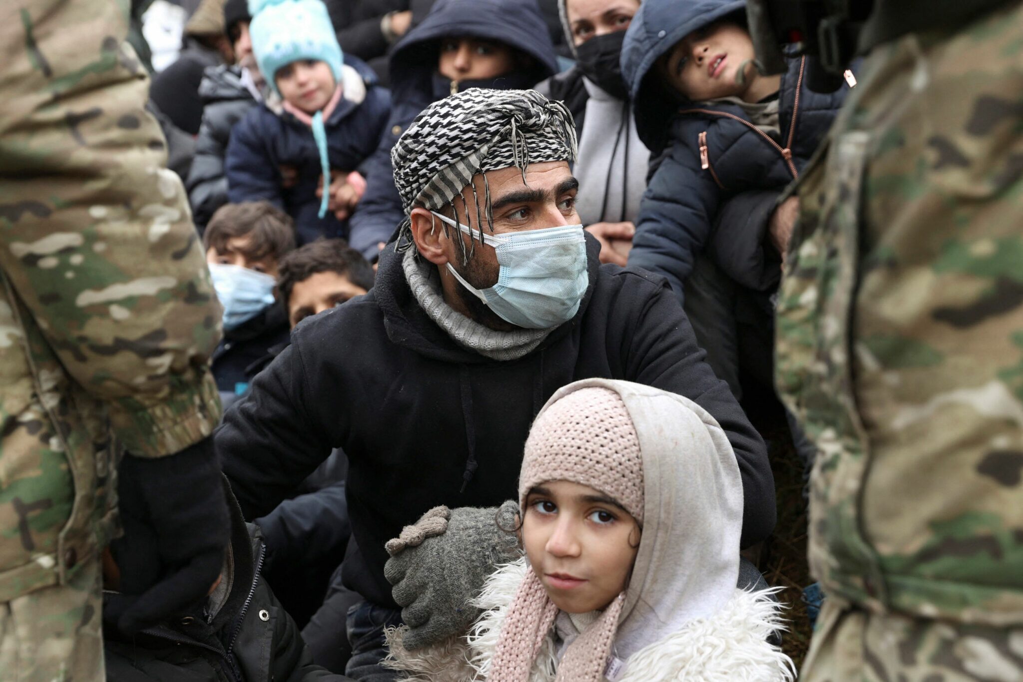 TOPSHOT - A group of migrants stands in front of Belarusian servicemen as they gather for the distribution of humanitarian aid in a camp near the Belarusian-Polish border in the Grodno region on November 14, 2021. Dozens of migrants have been detained after crossing into Poland from Belarus, Warsaw said on November 14, warning of a possible larger breakthrough ahead of an EU meeting to widen sanctions on Belarus. - Belarus OUT (Photo by Oksana MANCHUK / BELTA / AFP)