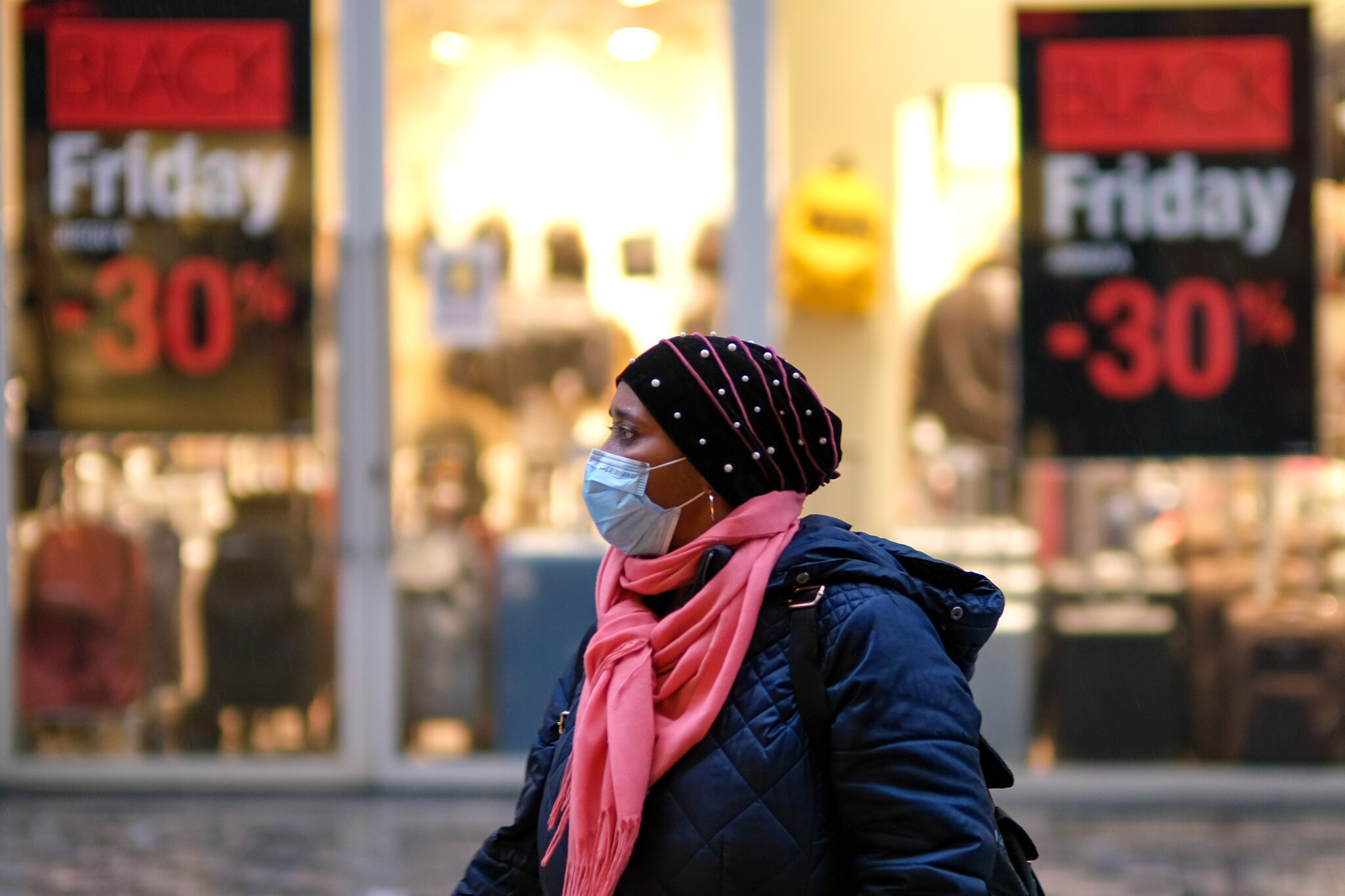 (211127) -- BRUSSELS, Nov. 27, 2021 (Xinhua) -- A woman wearing a face mask walks past posters about "Black Friday" in Brussels, Belgium, Nov. 26, 2021. The annual "Black Friday" sales attracted lots of customers though the COVID-19 situation in Belgium was still tough. From Nov. 16 to 22, a total of 16,762 new infections were registered daily, a 48 percent week-on-week increase, the Sciensano public health institute said. (Xinhua/Zhang Cheng)