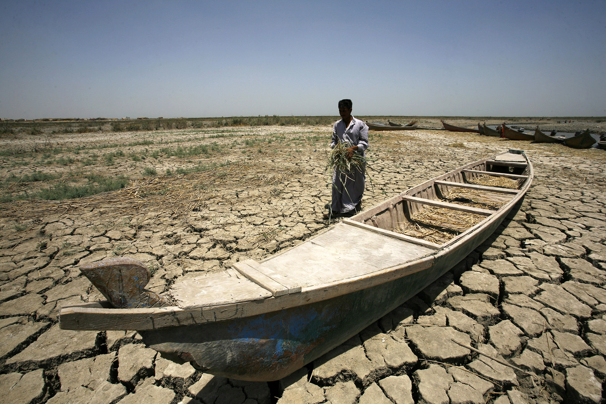 An Iraqi man walks past a canoe siting on dry, cracked earth in the Chibayish marshes near the southern Iraqi city of Nasiriyah on June 25, 2015. Marsh areas in southern Iraq have been affected since the Islamic State group started closing the gates of a dam on the Euphrates River in the central city of Ramadi, which is under the jihadist group's control. AFP PHOTO / HAIDAR HAMDANI (Photo by HAIDAR HAMDANI / AFP)