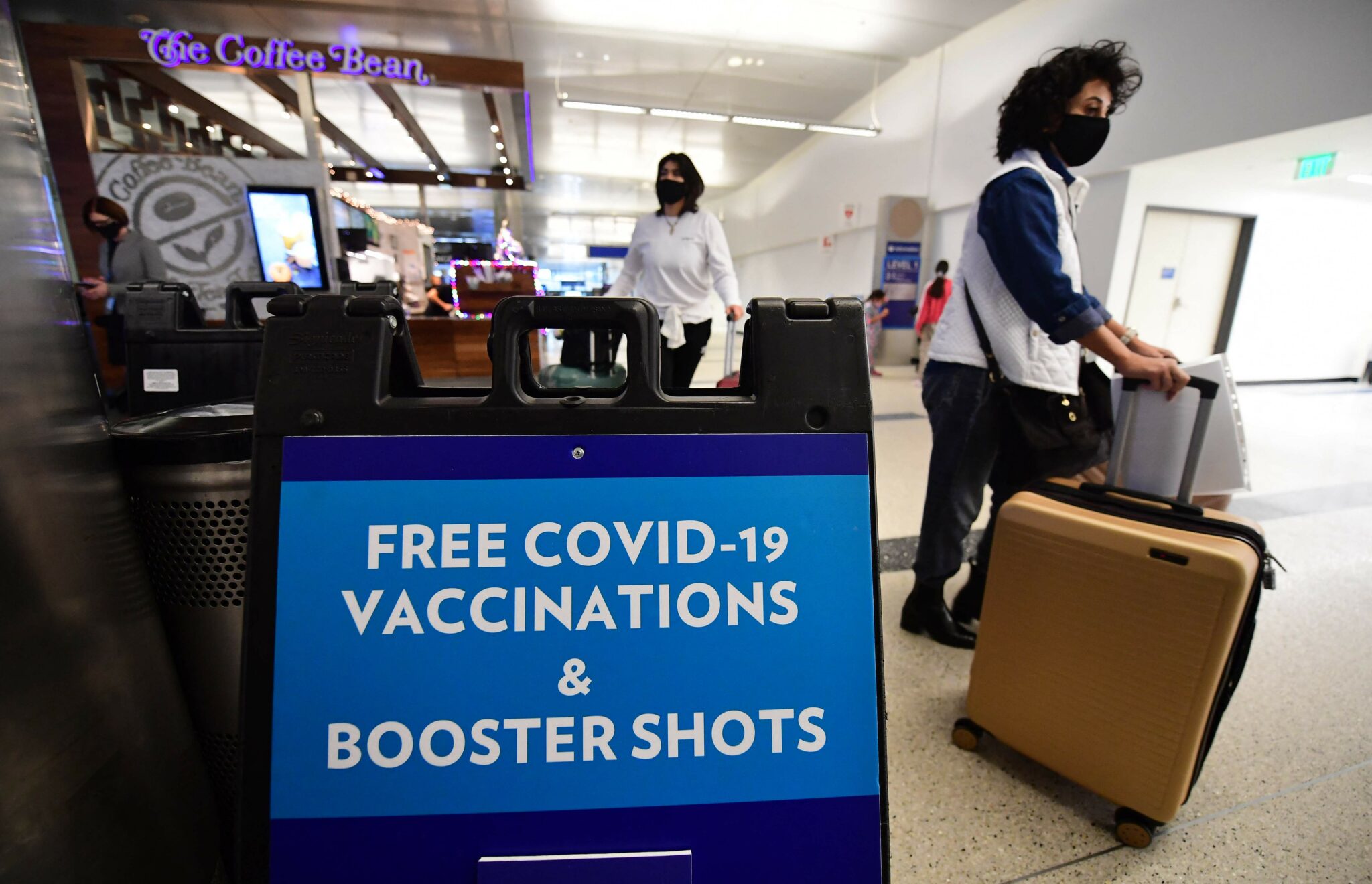 Travelers walk past a sign offering free Covid-19 vaccinations and booster shots at a pop-up clinic in the international arrivals area of Los Angeles International Airport in Los Angeles, California on December 22, 2021. The clinic at the airport offers free vaccinations and boosters for holiday travelers on December 22 and on December 29. Los Angeles County sees what could be the beginning of a winter surge with more than 3,200 Covid-19 cases reported every day since last December 17. (Photo by Frederic J. BROWN / AFP)