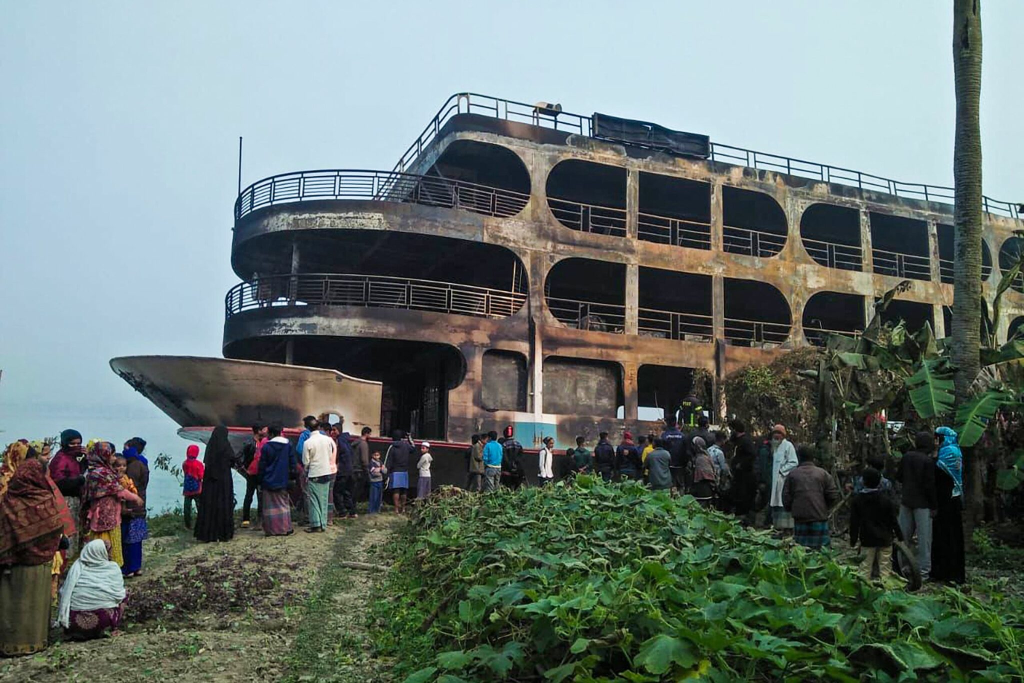 Villagers look at a burnt-out ferry after it caught on fire killing at least 37 people in Jhakakathi, 250 kilometres (160 miles) south of Dhaka, on December 24, 2021. (Photo by AFP)