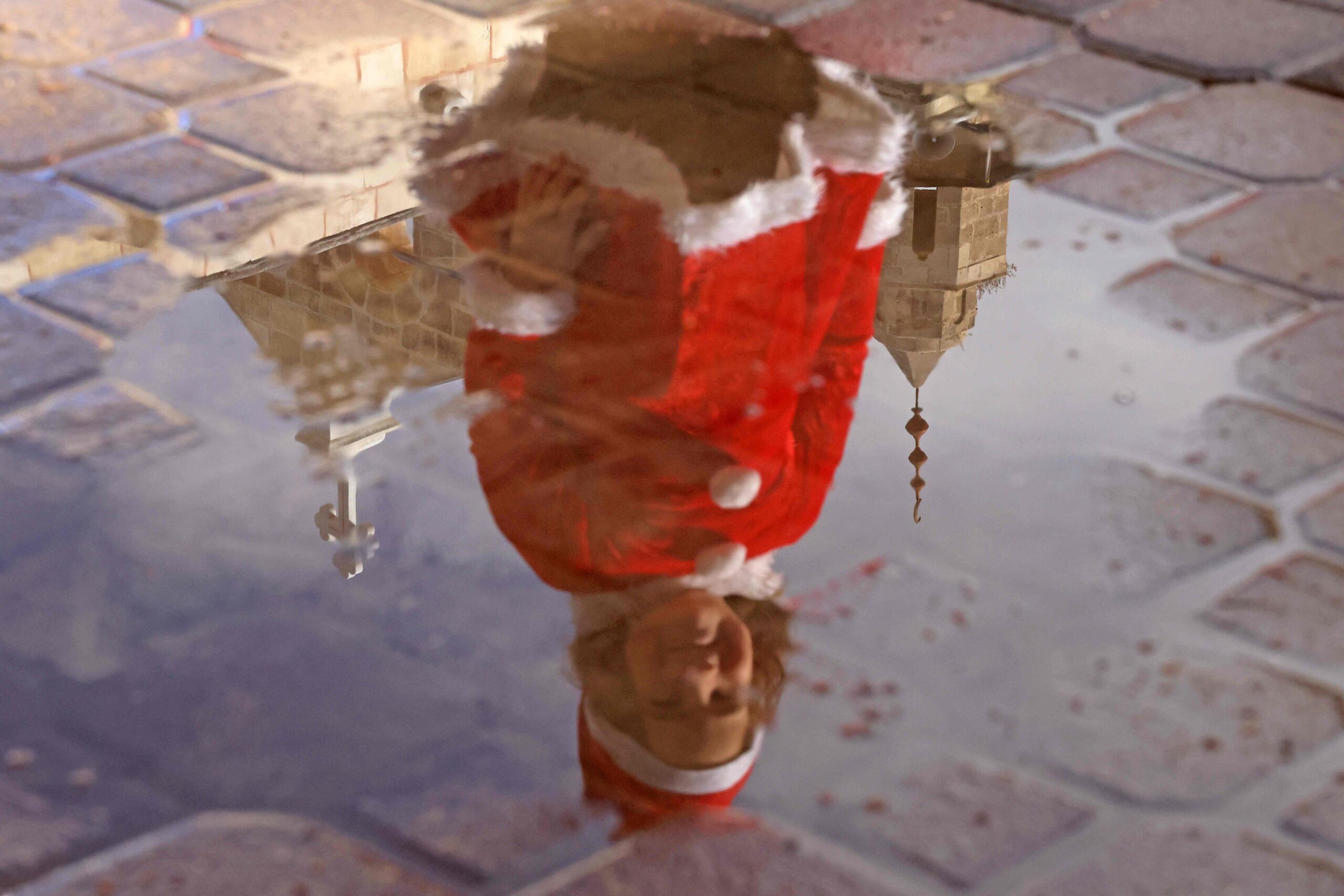 A Palestinian girl, dressed as Santa Claus, is reflected in a puddle outside the Church of Saint Porphyrius during Christmas celebrations in Gaza City, on December 24, 2021. (Photo by MOHAMMED ABED / AFP)