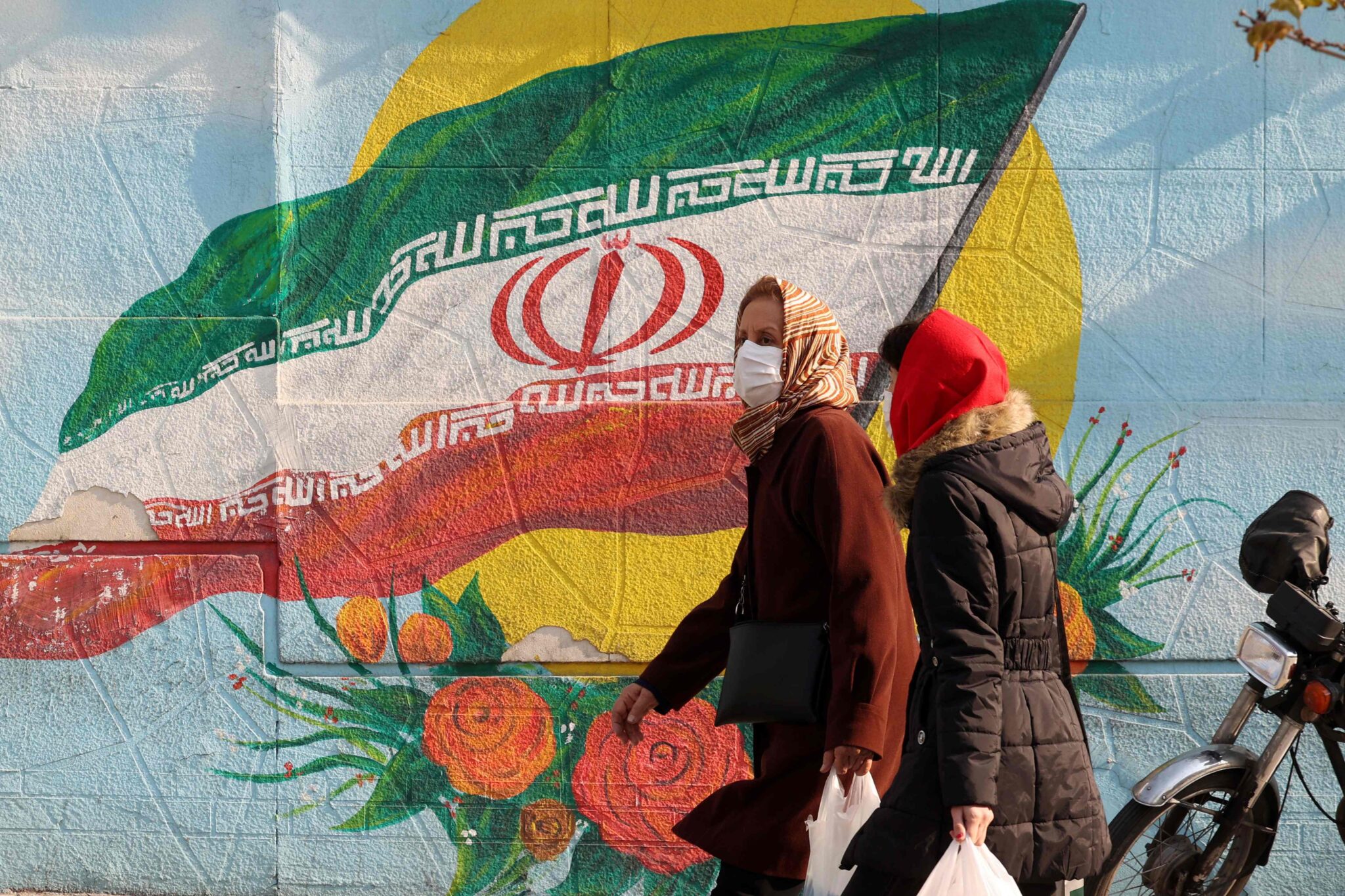 Iranians walk down a street in the capital Tehran on December 28, 2021. (Photo by ATTA KENARE / AFP)