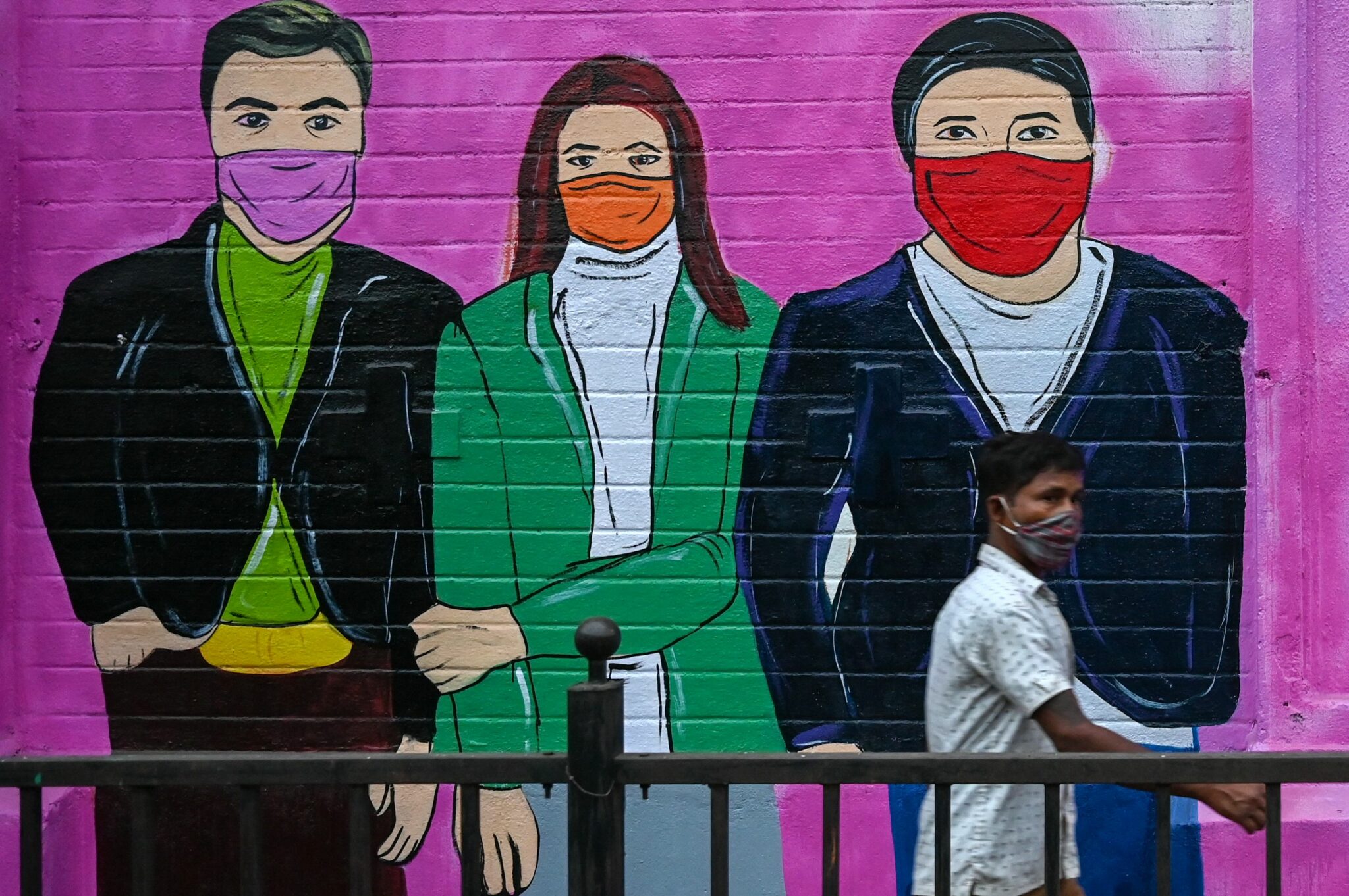 A pedestrian walks past a wall mural depicting a family to spread awareness about the Covid-19 coronavirus in Mumbai on November 30, 2021. (Photo by Punit PARANJPE / AFP)