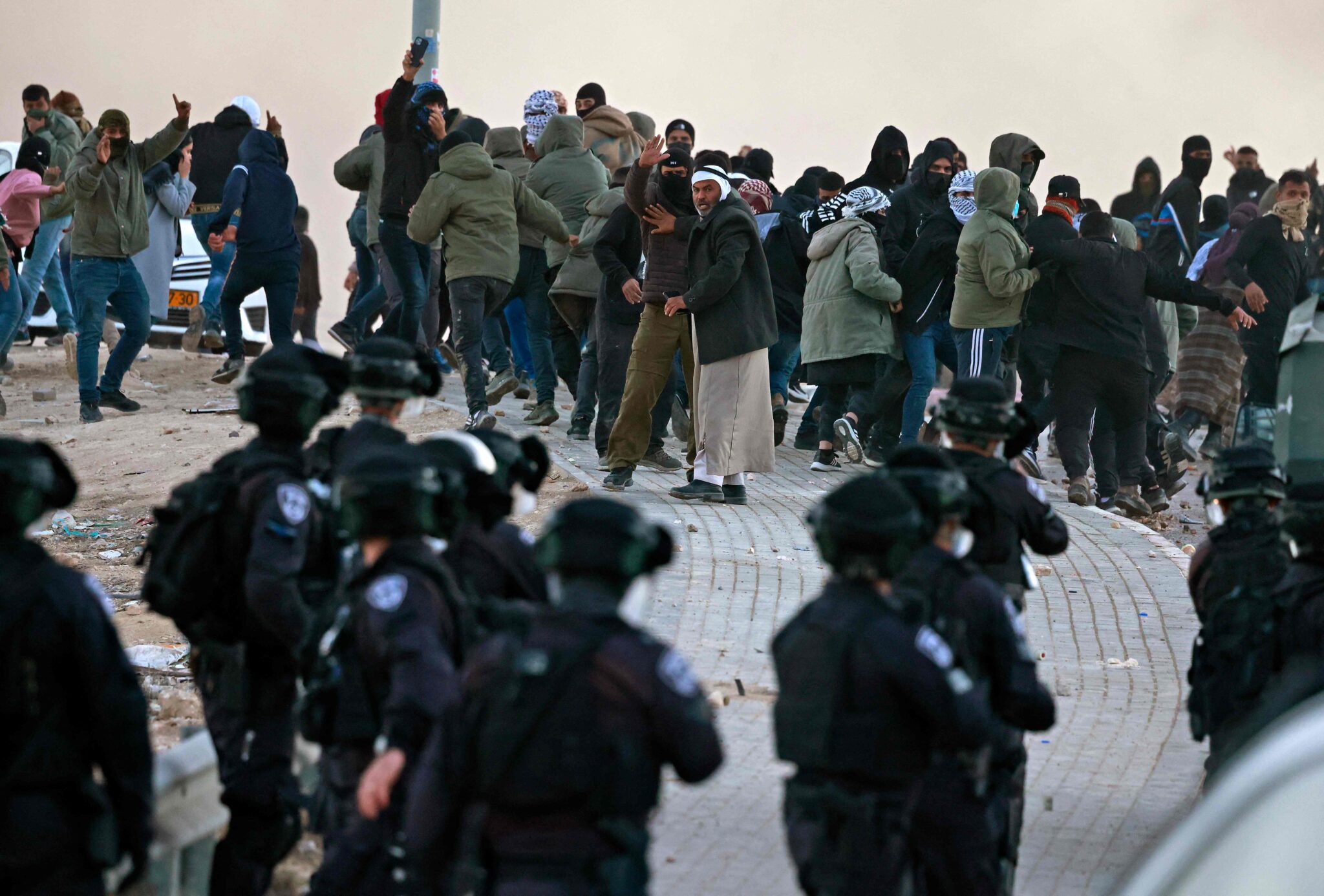 Israeli forces face Beduin demonstrators as they clash during a protest in the southern Israeli village of Sawe al-Atrash in the Neguev Desert against an afforestation project by the Jewish National Fund (JNF), on January 13, 2022. Bedouin, who are part of Israel's 20 percent Arab minority, have long opposed tree-planting initiatives in the Negev, blasting them as a de facto government land grab in areas they call home. (Photo by Menahem KAHANA / AFP)