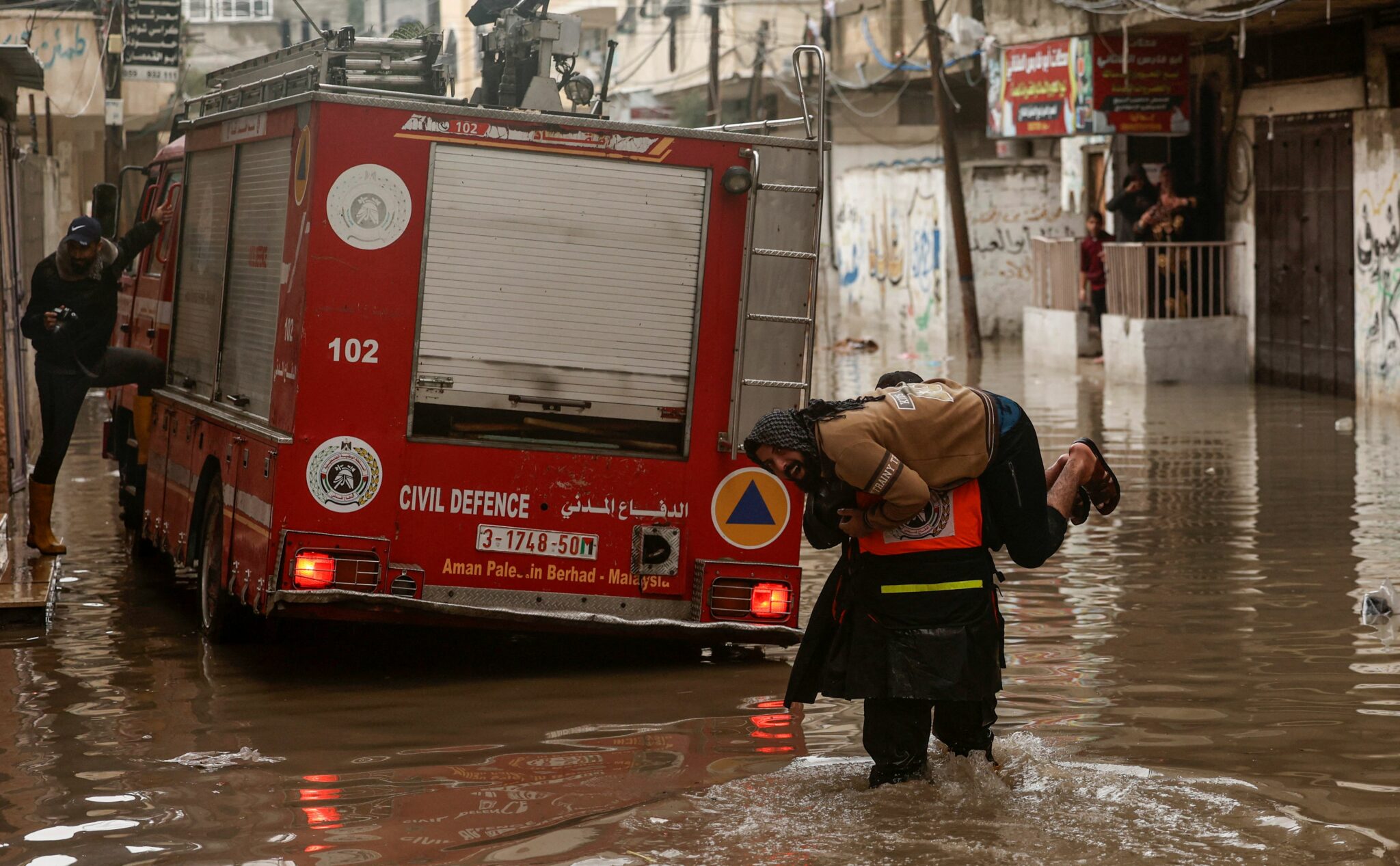 A Palestinian firefighter carries a man on his shoulder after evacuating him from an inundated house, following torrential rains that hit the Jabalia refugee camp in the northern Gaza strip, on January 16, 2022. (Photo by Mahmud HAMS / AFP)