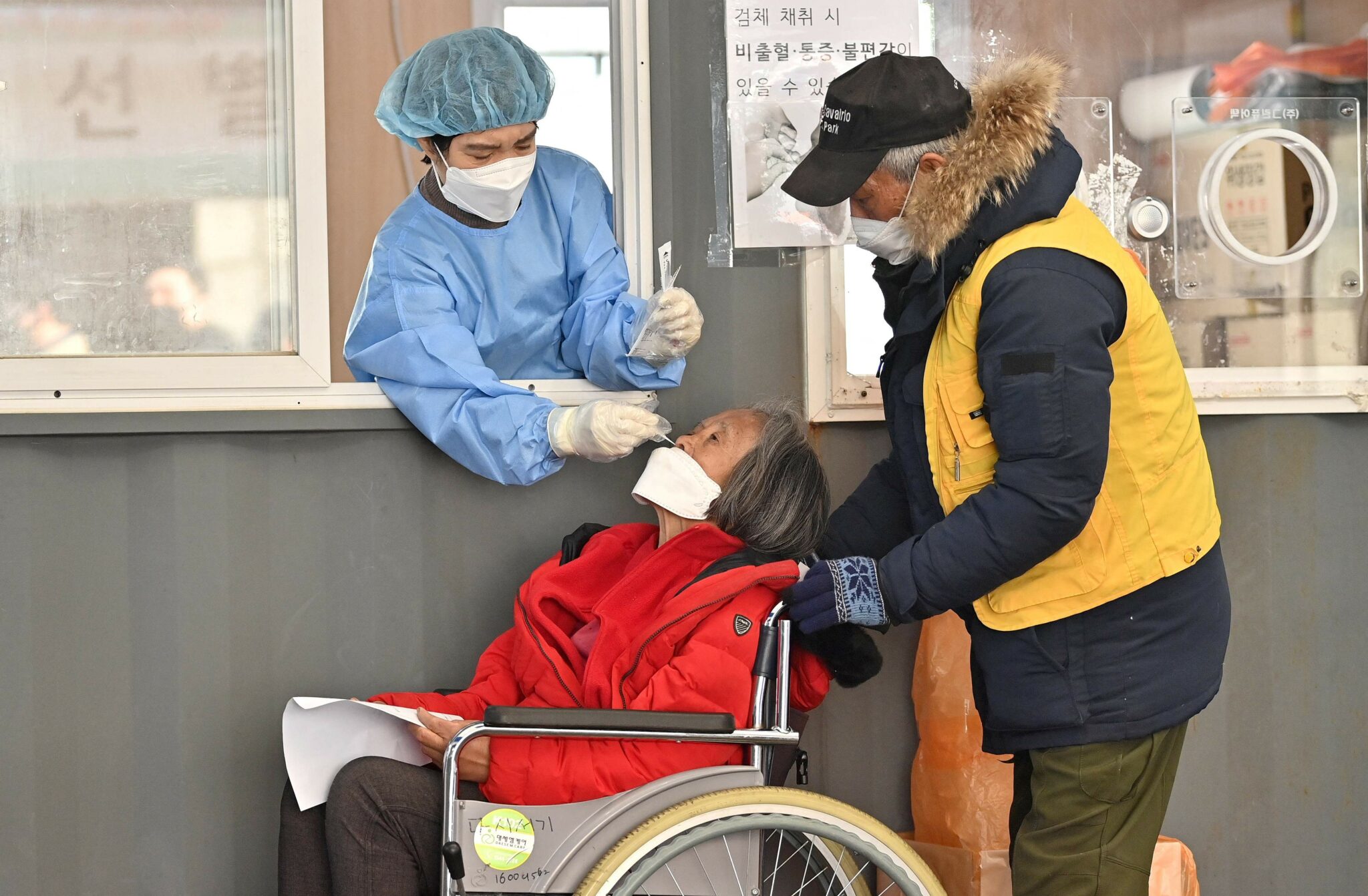 A medical staff member (L-in booth) takes a nasal swab from a visitor as part of a test for the Covid-19 coronavirus at a virus testing centre in Seoul on January 26, 2022. (Photo by Jung Yeon-je / AFP)