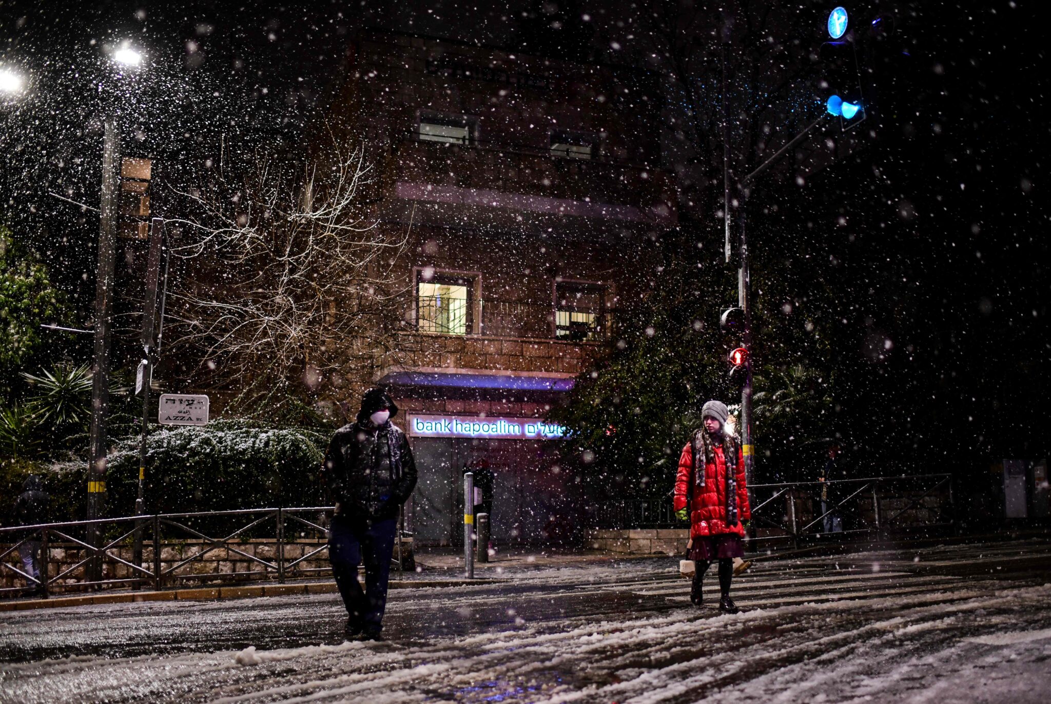 People are pictured in a street during snowfall in Jerusalem, on January 26, 2022. (Photo by RONALDO SCHEMIDT / AFP)