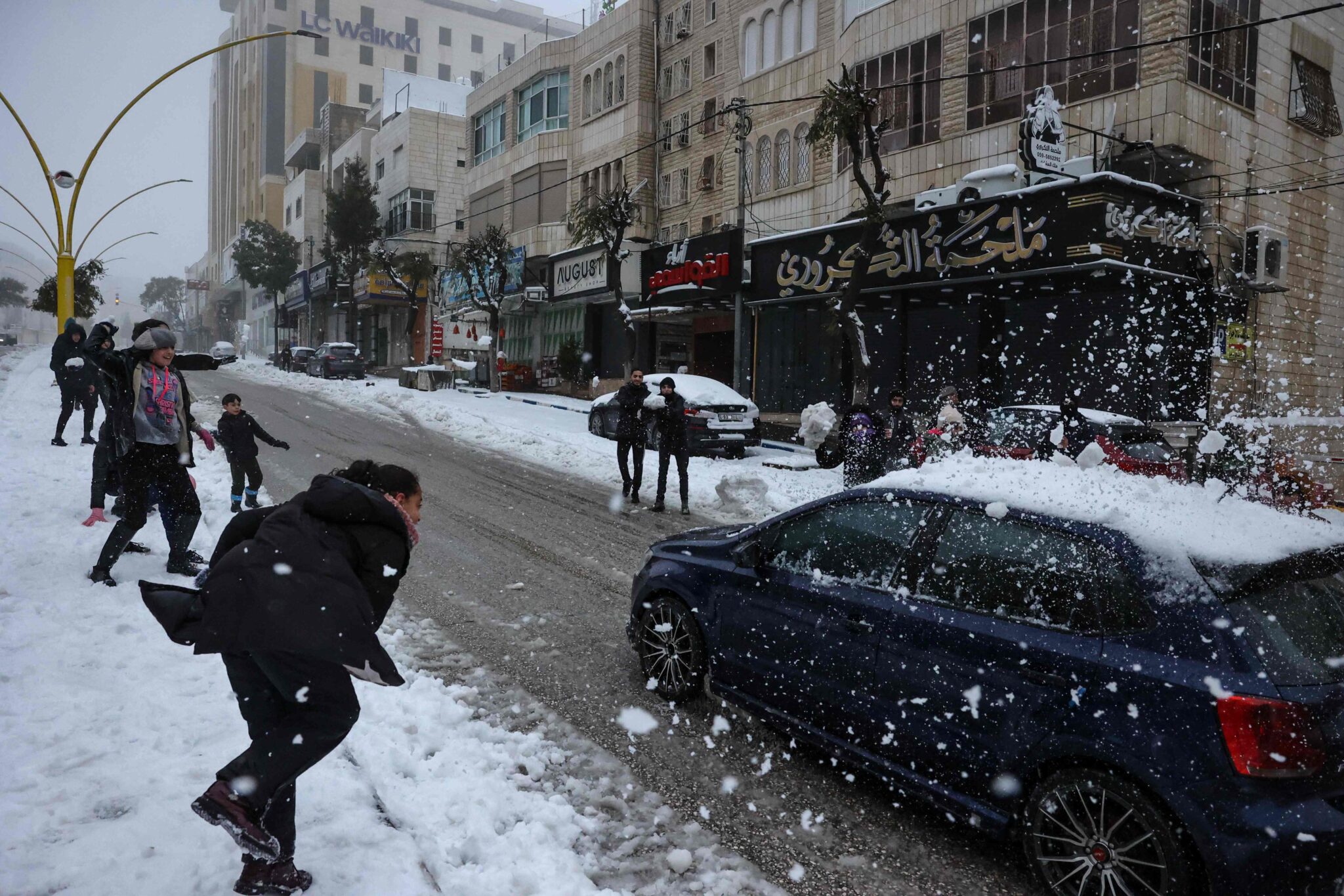 Palestinian children throw snowballs at a passing car following an overnight snow fall in the occupied West Bank town of Hebron, on January 27, 2022. (Photo by HAZEM BADER / AFP)