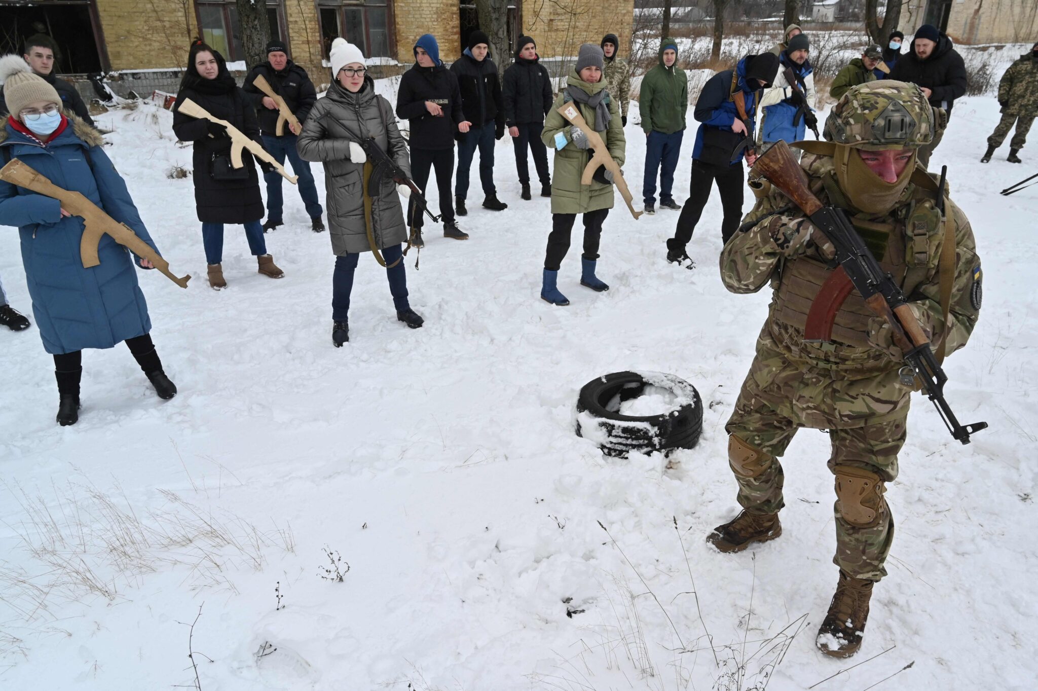 A military instructor teaches civilians holding wooden replicas of Kalashnikov rifles, during a training session at an abandoned factory in the Ukrainian capital of Kyiv on January 30, 2022. As fears grow of a potential invasion by Russian troops massed on Ukraine's border, within the framework of the training there were classes on tactics, paramedics, training on the obstacle course. The training is conducted by instructors with combat experience, members of the public initiative "Total Resistance". (Photo by Sergei SUPINSKY / AFP)