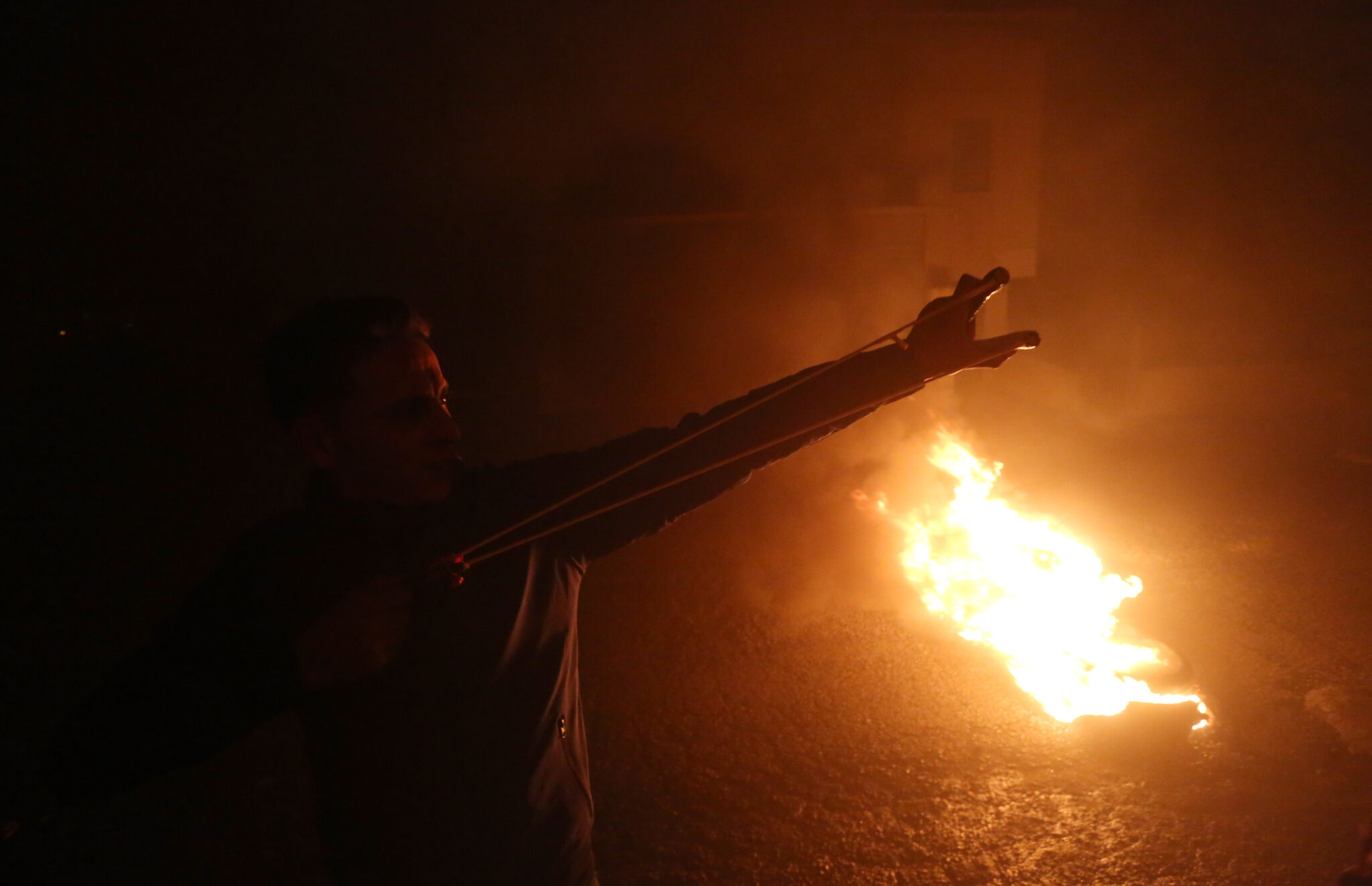 (220113) -- NABLUS, Jan. 13, 2022 (Xinhua) -- A Palestinian protester uses a slingshot to hurl a stone at Israeli soldiers during clashes in the village of Burqa near the West Bank city of Nablus, on Jan. 13, 2022. (Photo by Ayman Nobani/Xinhua)