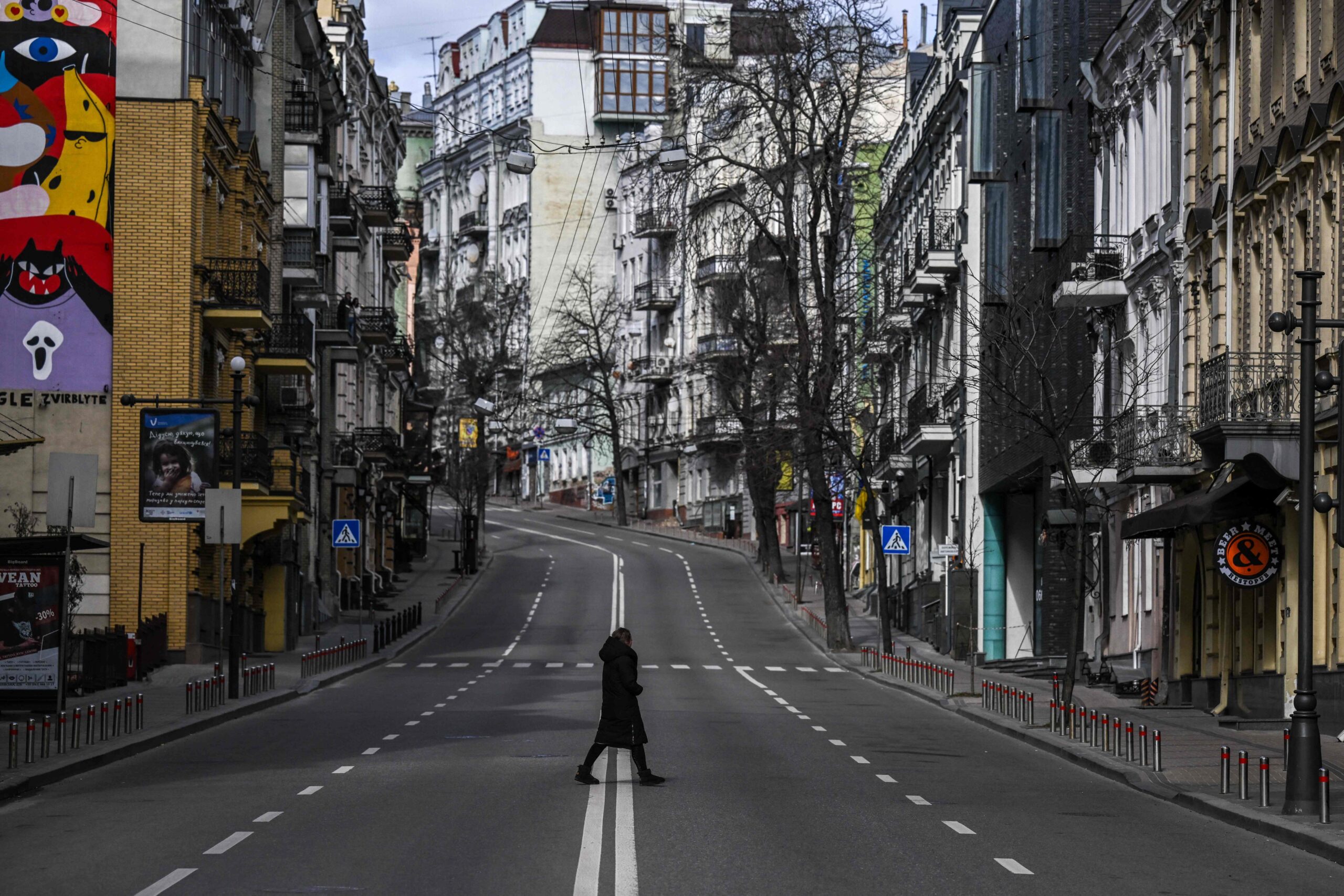 TOPSHOT - A civilian crosses an empty street in downtown Kyiv, on February 27, 2022. Kyiv authorities on February 26, 2022 toughened curfew orders in the city, saying violators would be considered "enemy" saboteurs as Russian forces press to capture Ukraine's capital. (Photo by Aris Messinis / AFP)