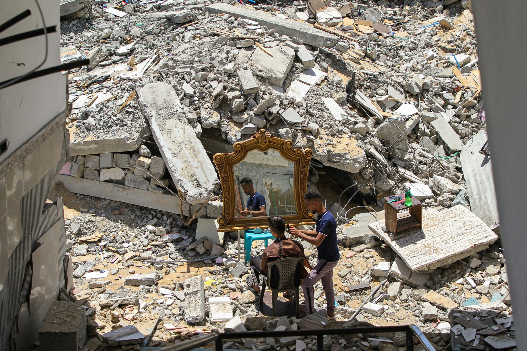 (220106) -- BEIJING, Jan. 6, 2022 (Xinhua) -- Abdullah al-Zawara'a, 23, a Palestinian barber, works for a client for free near his house, which was destroyed in Israeli airstrikes in the northern Gaza Strip town of Beit Lahia, May 26, 2021. (Photo by Rizek Abdeljawad/Xinhua)