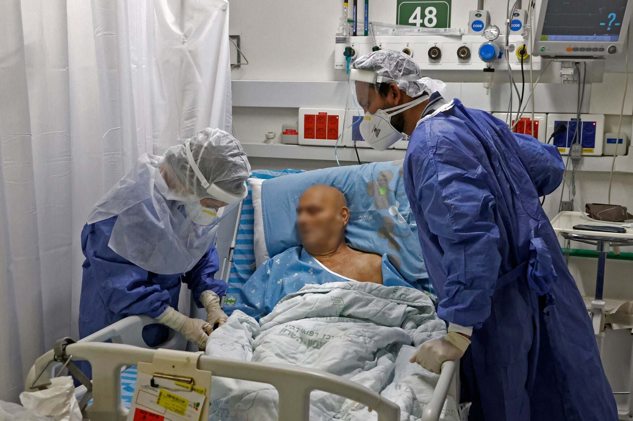 Medical staff members wearing protective gear tend to a coronavirus patient in the COVID-19 ward at Beilinson Hospital Rabin Medical Centre in Israel's central city of Petah Tikva on February 1, 2022. The facility was originally built as an underground parking lot before being converted into a medical centre to receive coronavirus patients as cases spiked. (Photo by JACK GUEZ / AFP)