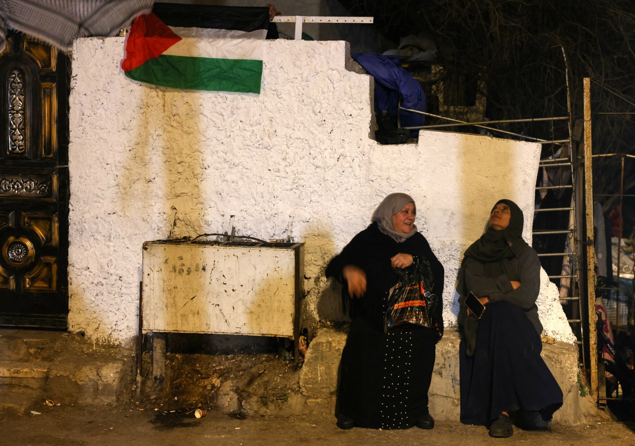 Palestinian women sit against a wall in the east Jerusalem neighbourhood of Sheikh Jarrah, on March 2, 2022. Israel's Supreme Court yesterday froze the eviction of four Palestinian families from the flashpoint east Jerusalem neighbourhood of Sheikh Jarrah, where Jewish settler groups have sought to seize control. (Photo by AHMAD GHARABLI / AFP)