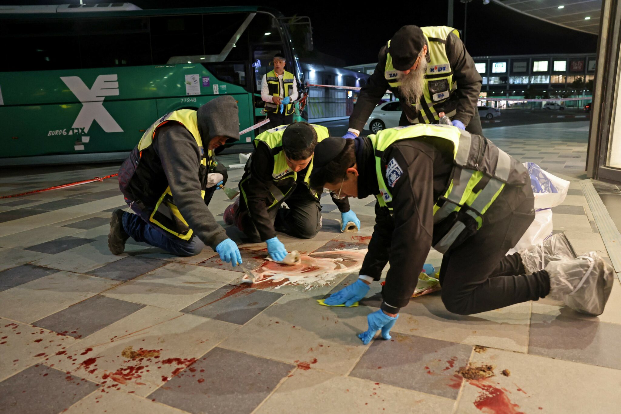 TOPSHOT - Zaka volunteers, an Ultra-Orthodox Jewish emergency response team in Israel, clean up blood stains at the scene of a knife attack outside a shopping centre in the southern city of Beersheba, on March 22, 2022. A knife and car-ramming attack in southern Israel killed at least three people and wounded several others, in what police described as a suspected "terrorist attack". (Photo by AHMAD GHARABLI / AFP)