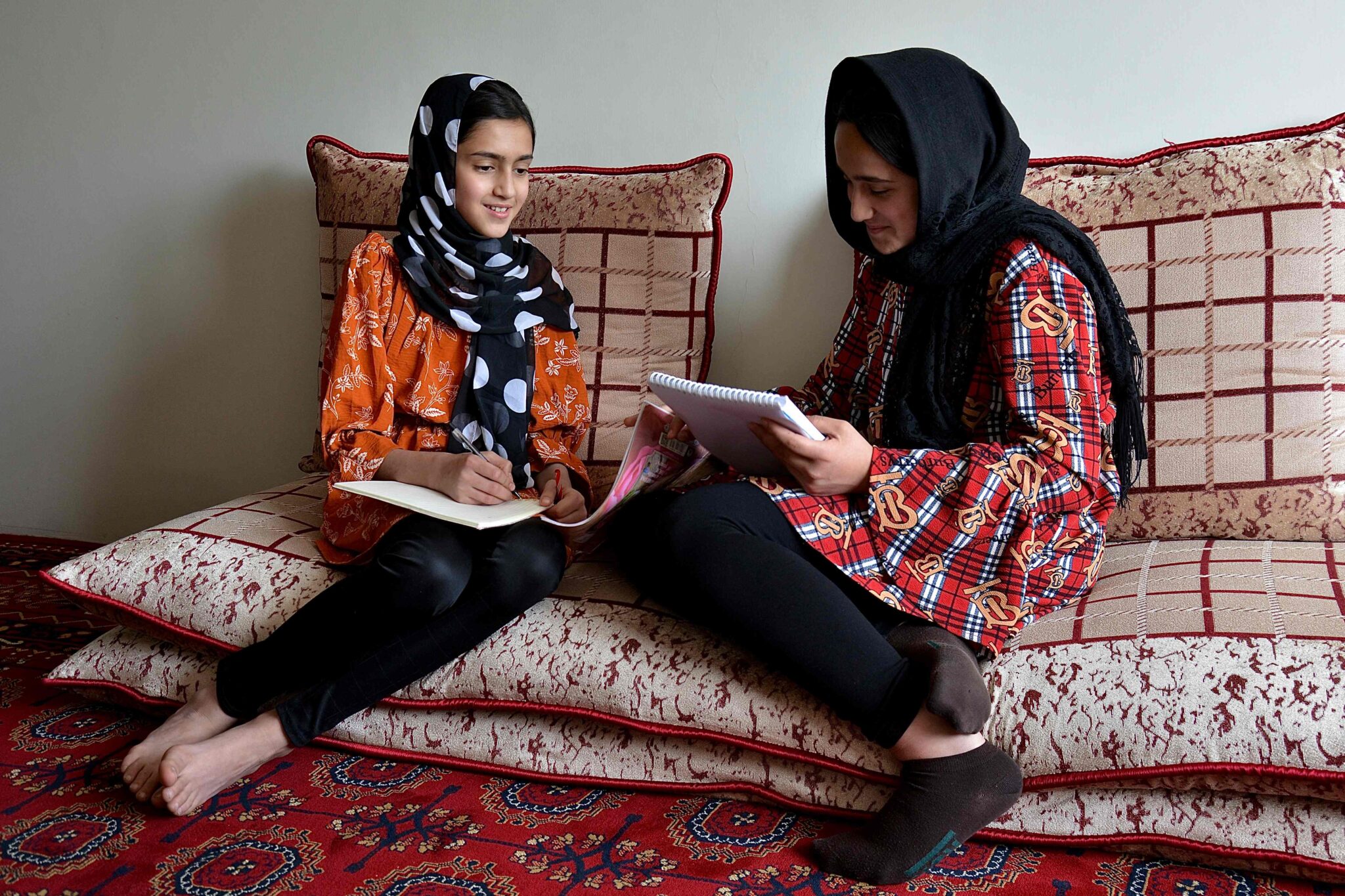 In this photograph taken on March 24, 2022, school girls Malahat Haidari (L) and her sister Adeeba Haidari study at their home in Kabul. Days after the Taliban staged a cruel U-turn on allowing Afghan girls back to school, Adeeba Haidari feels as if she is back in prison. (Photo by Ahmad SAHEL ARMAN / AFP)