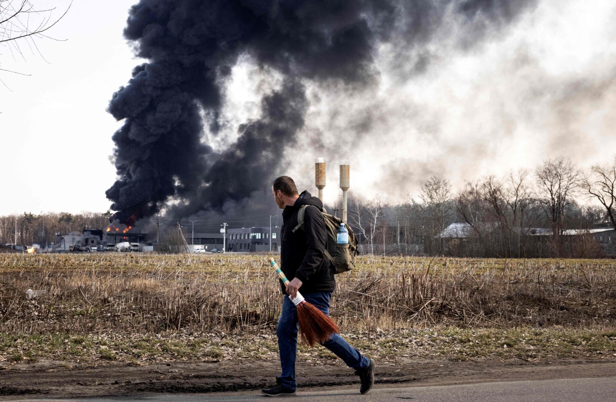 A man walks while smoke rises after Russian attacks hit a fuel storage facility in the city of Kalynivka, on March 25, 2022. (Photo by FADEL SENNA / AFP)