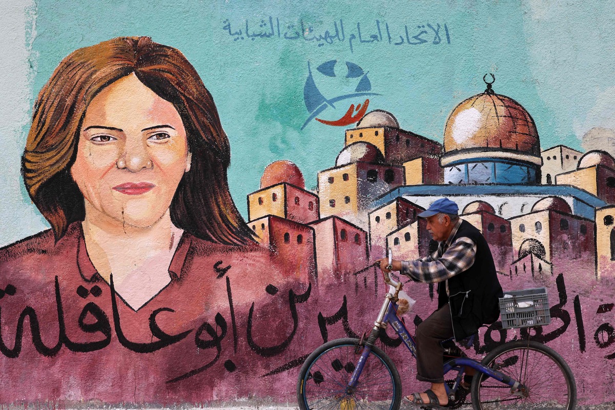 A Palestinian man rides his bicycle in front of a mural painted by an artist in honour of slain veteran Al-Jazeera journalist Shireen Abu Akleh, in Gaza City on May 13, 2022. Abu Akleh, who was shot dead on May 11, 2022 while covering a raid in the Israeli-occupied West Bank, was among Arab media's most prominent figures and widely hailed for her bravery and professionalism. (Photo by MOHAMMED ABED / AFP)