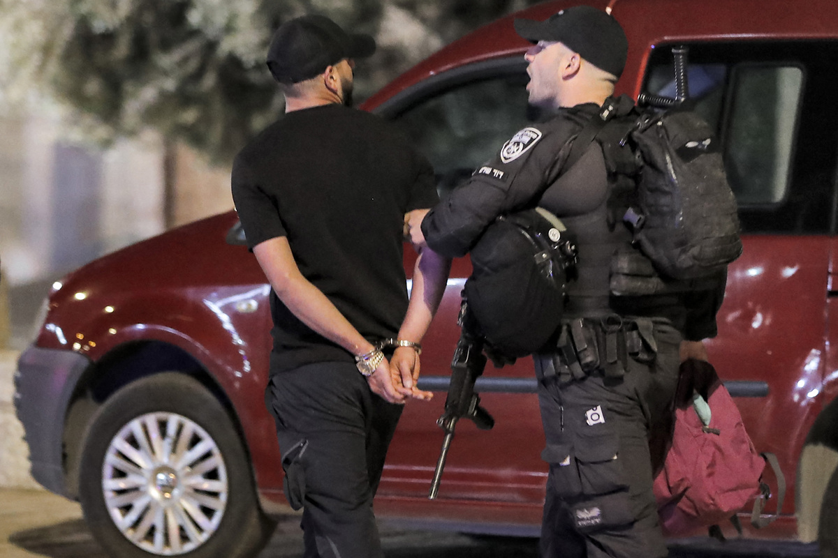 An Israeli policeman escorts a detained and handcuffed man at the scene of a stabbing attack at the Damascus Gate of the Old City of Jerusalem on May 8, 2022. (Photo by Ahmad GHARABLI / AFP)