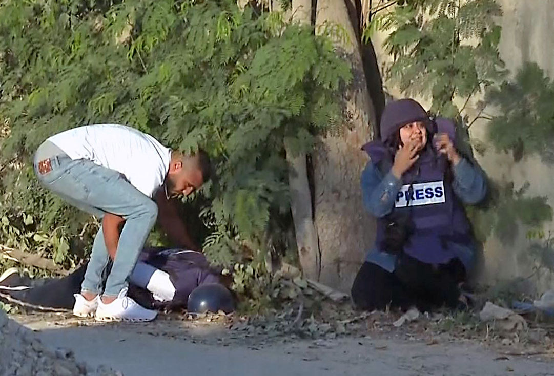 EDITORS NOTE: Graphic content / An image grab from footage distributed by the Doha-based Al-Jazeera TV shows a reporter reacting (R) as an unidentified man tries to lift the body of the channel's veteran journalist Shireen Abu Aqleh from the ground after she was fatally wounded by gunfire in Jenin in the occupied West Bank on May 11, 2022. Abu Aqleh, 51, a prominent figure in the channel's Arabic news service was shot dead by Israeli troops early in the morning as she covered a raid on Jenin refugee camp in the occupied West Bank, according to Al-Jazeera. The Qatari news channel said its journalist had been shot dead "deliberately" and "in cold blood" by Israeli troops but Israeli Prime Minister Naftali Bennett said it was likely Palestinian gunfire had killed the reporter. - RESTRICTED TO EDITORIAL USE - MANDATORY CREDIT "AFP PHOTO / Al-Jazeera" - NO MARKETING NO ADVERTISING CAMPAIGNS - DISTRIBUTED AS A SERVICE TO CLIENTS (Photo by AL JAZEERA / AFP) / RESTRICTED TO EDITORIAL USE - MANDATORY CREDIT "AFP PHOTO / Al-Jazeera" - NO MARKETING NO ADVERTISING CAMPAIGNS - DISTRIBUTED AS A SERVICE TO CLIENTS