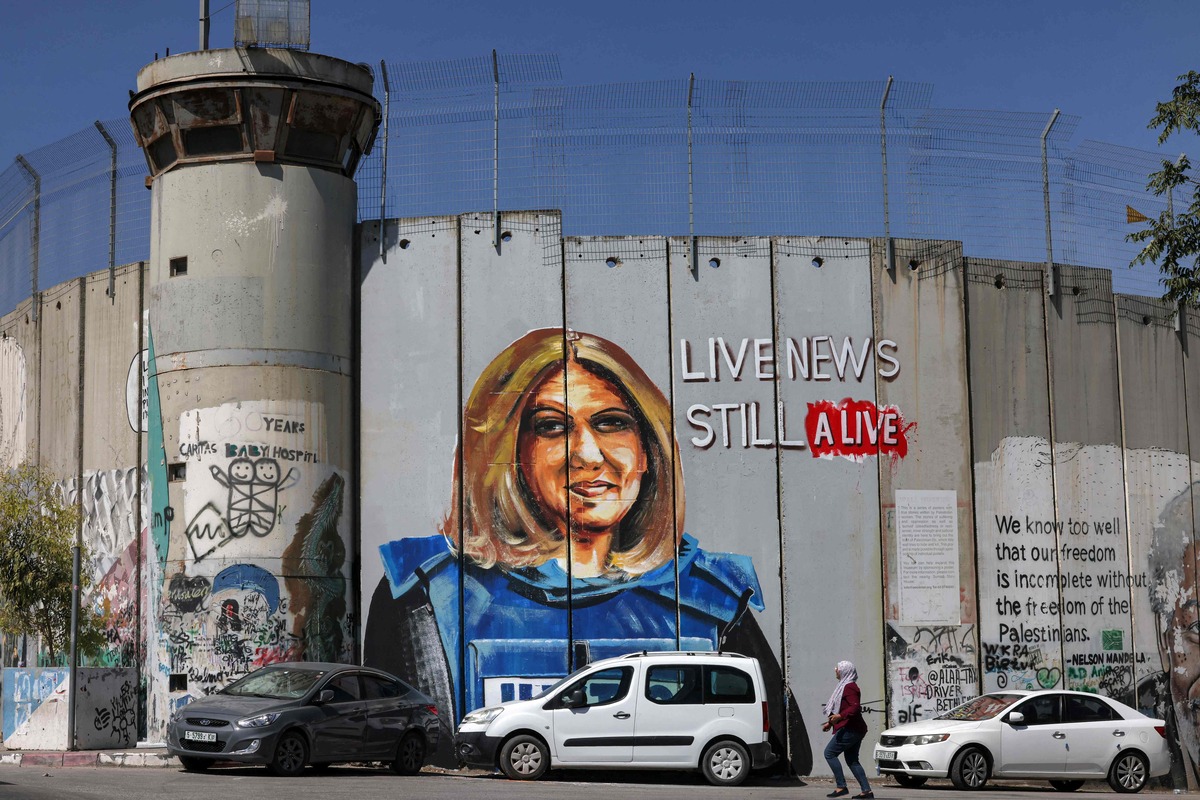 A woman walks past a mural depicting slain Al Jazeera journalist Shireen Abu Akleh, who was killed while covering an Israeli army raid in Jenin in May, drawn along Israel's controversial separation barrier in the biblical city of Bethlehem in the occupied West Bank on July 6, 2022. (Photo by AHMAD GHARABLI / AFP)