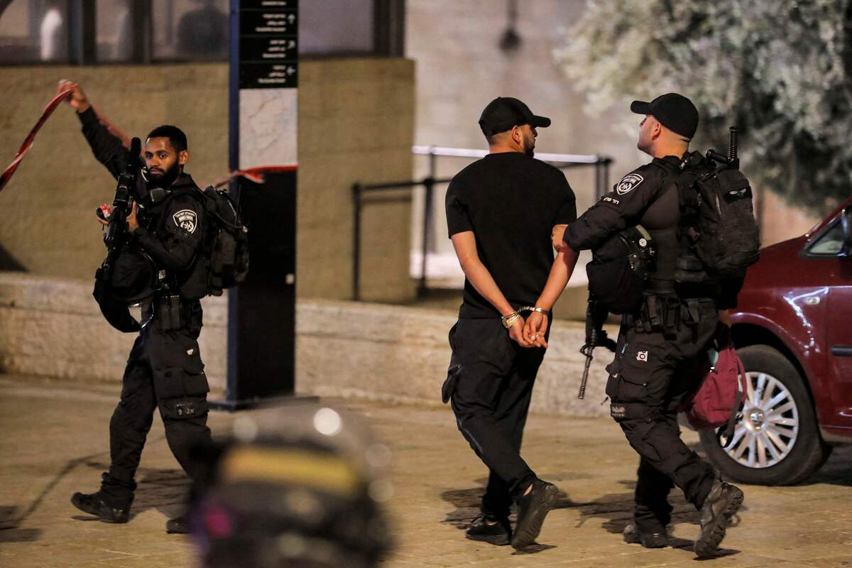 An Israeli policeman escorts a detained and handcuffed man at the scene of a stabbing attack at the Damascus Gate of the Old City of Jerusalem on May 8, 2022. (Photo by Ahmad GHARABLI / AFP)