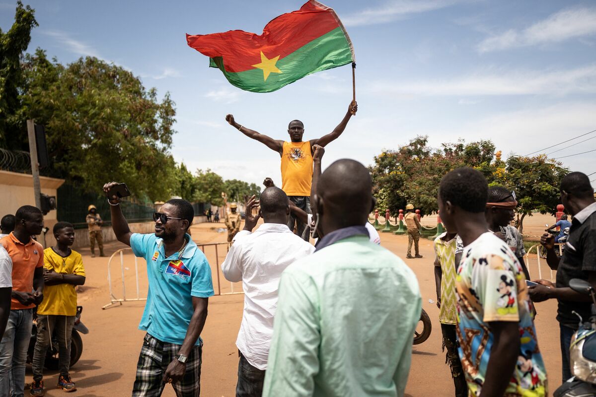 TOPSHOT - A man waves a Burkina Faso flag as others demonstrate while Burkina Faso soldiers are seen deployed in Ouagadougou on September 30, 2022. Shots rang out before dawn on Friday around Burkina Faso's presidential palace and headquarters of the military junta, which itself seized power in a coup last January. The government said the developing situation was linked to an "internal crisis in the army", after AFP journalists saw troops block several main roads in the capital Ouagadougou. (Photo by Olympia DE MAISMONT / AFP)