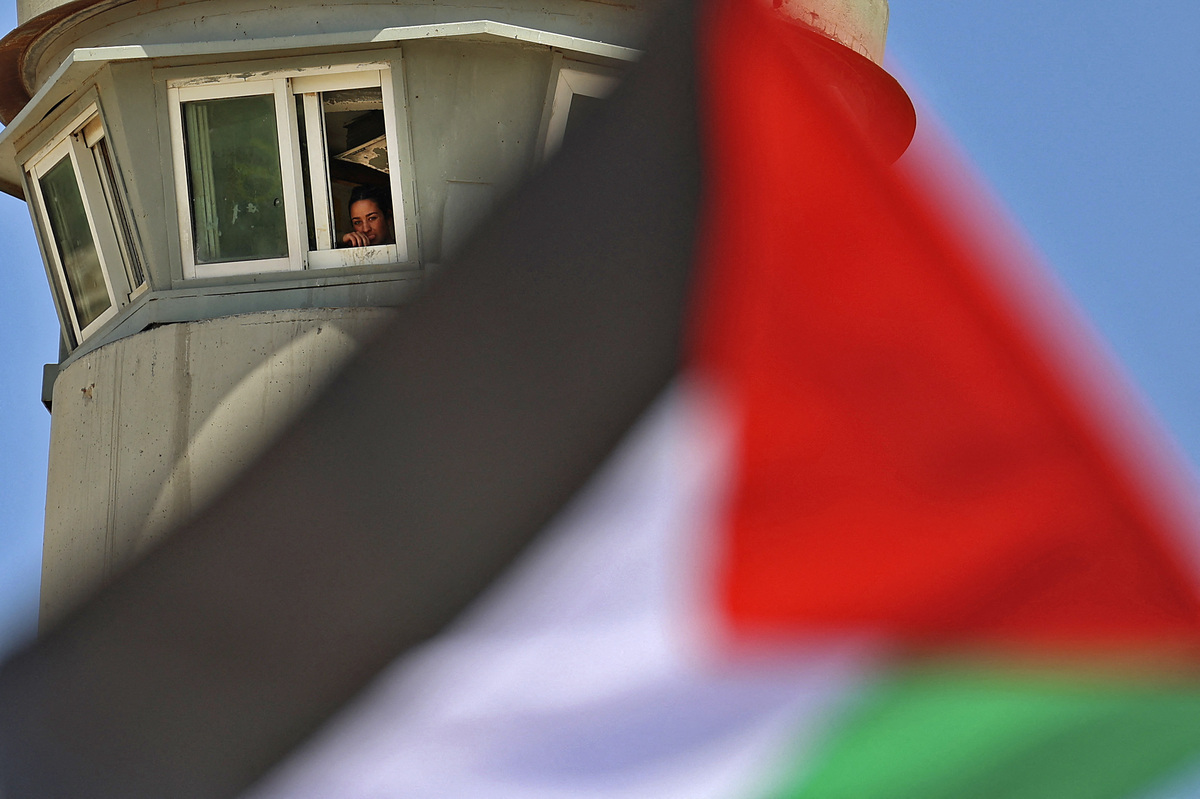 An Isreali soldier watches from a tower as Palestinian demonstrators wave the national flag in the city of Tubas on June 6, 2022, during a gathering to denounce the Israeli settlement expansion in the Jordan Valley. (Photo by JAAFAR ASHTIYEH / AFP)