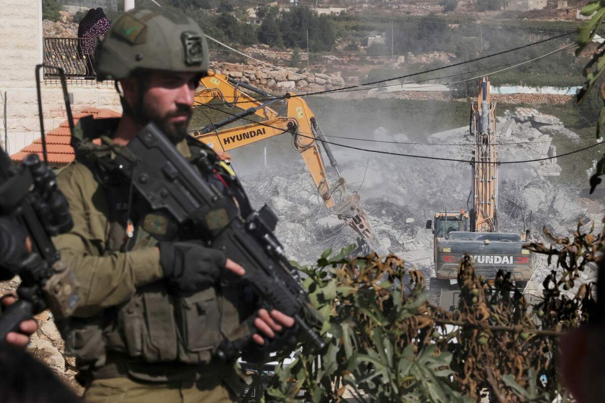 Israeli forces stand guard around a building being demolished by army bulldozers in the Palestinian city of Hebron, in the occupied West Bank on October 31, 2022. Israel regularly razes homes built by Palestinians in east Jerusalem and the occupied West Bank if they lack the relevant construction permits. The catch, according to an UN study, is that such permits are "virtually impossible" to obtain, and the result is a chronic housing shortage. (Photo by HAZEM BADER / AFP)