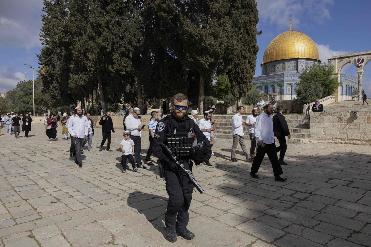 An Israeli security guard escorts a group of religious Jewish men and women during their visit to the Temple Mount, which is known to Muslims as the Haram al-Sharif (The Noble Sanctuary), at the Al-Aqasa mosques compound in the old city of Jerusalem on April 20, 2022. Hundreds of Jewish pilgrims escorted by Israeli police visit the site during the Pesach holiday as Jews are allowed to visit at certain times, but they are prohibited from praying there. Incidents at the Al-Aqsa mosque compound, the holiest site in Judaism and the third-holiest in Islam, have triggered repeated rounds of violence over the past century. (Photo by MENAHEM KAHANA / AFP)