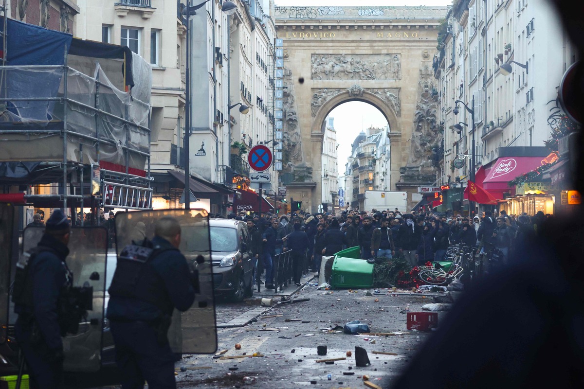 TOPSHOT - Protestors clashes with French riot police officers following a statement by French Interior Minister Gerald Darmanin (unseen) at the site where several shots were fired along rue d'Enghien in the 10th arrondissement, in Paris on December 23, 2022. Three people were killed and three injured in a shooting in central Paris on December 23, 2022, police and prosecutors said, adding that the shooter, in his 60s, had been arrested. The motives of the gunman remain unclear, with two of the four injured left in a serious condition, the French officials said. (Photo by Thomas SAMSON / AFP)