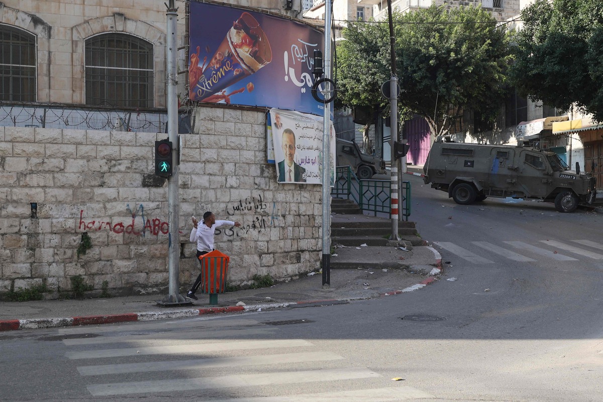 A Palestinian protester hurls rocks at armoured vehicles of Israeli security forces deploying during a raid in the old city of Nablus, in the occupied West Bank, on December 30, 2022. (Photo by JAAFAR ASHTIYEH / AFP)