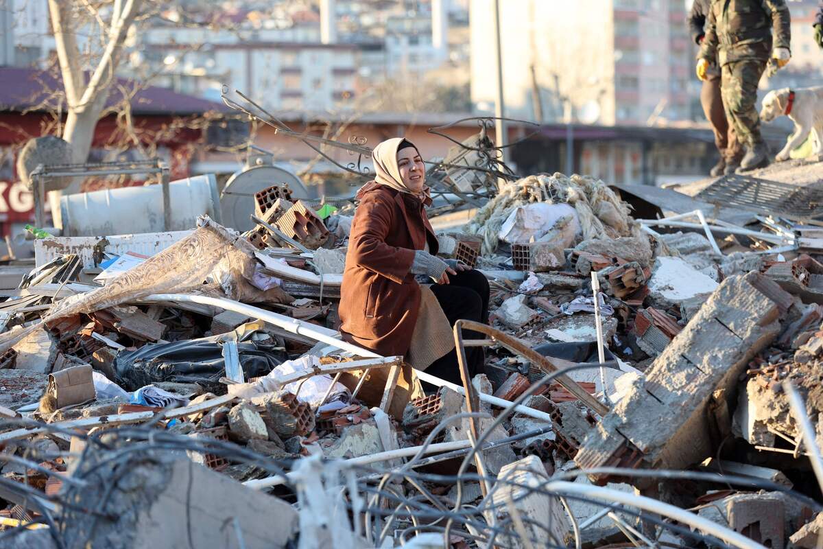 A woman sits on the rubble of a destroyed building in Kahramanmaras, southern Turkey, a day after a 7.8-magnitude earthquake struck the country's southeast, on February 7, 2023. Rescuers in Turkey and Syria braved frigid weather, aftershocks and collapsing buildings, as they dug for survivors buried by an earthquake that killed more than 5,000 people. Some of the heaviest devastation occurred near the quake's epicentre between Kahramanmaras and Gaziantep, a city of two million where entire blocks now lie in ruins under gathering snow. (Photo by Adem ALTAN / AFP)