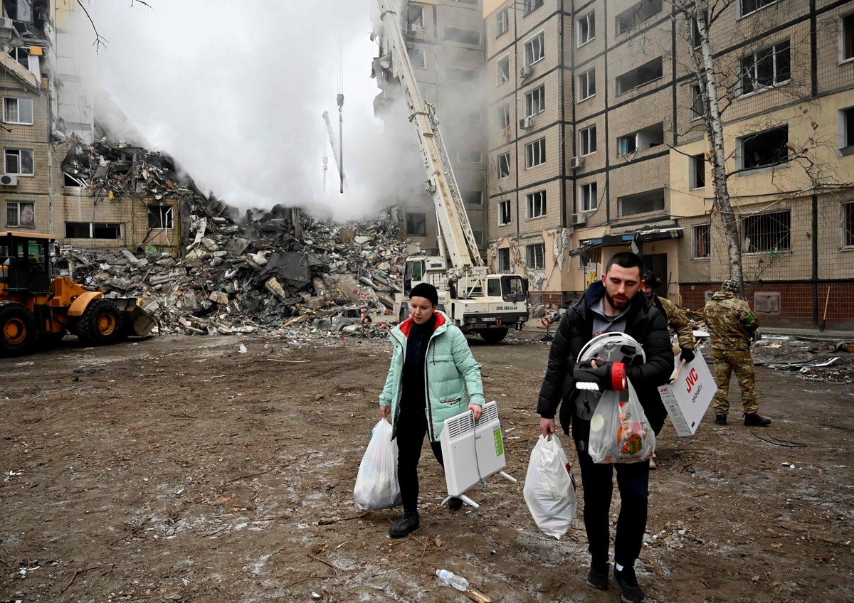 EDITORS NOTE: Graphic content / Residents carry their belongings from a residential building destroyed after a missile strike, in Dnipro on January 15, 2023, amid the Russian invasion of Ukraine. The death toll rose to at least 20 on January 15 after a strike on a residential building in Dnipro on January 14, a city in centre-east Ukraine, the Ukrainian regional governor said. (Photo by SERGEI CHUZAVKOV / AFP)