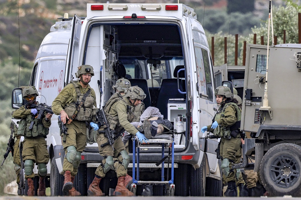 Israeli soldiers walk past an ambulance as they move a gurney carrying the body of a Palestinian, who was killed in clashes during an Israeli army operation, near the settlement of Elon Moreh in the occupied West Bank near Nablus on April 11, 2023. (Photo by Jaafar ASHTIYEH / AFP)