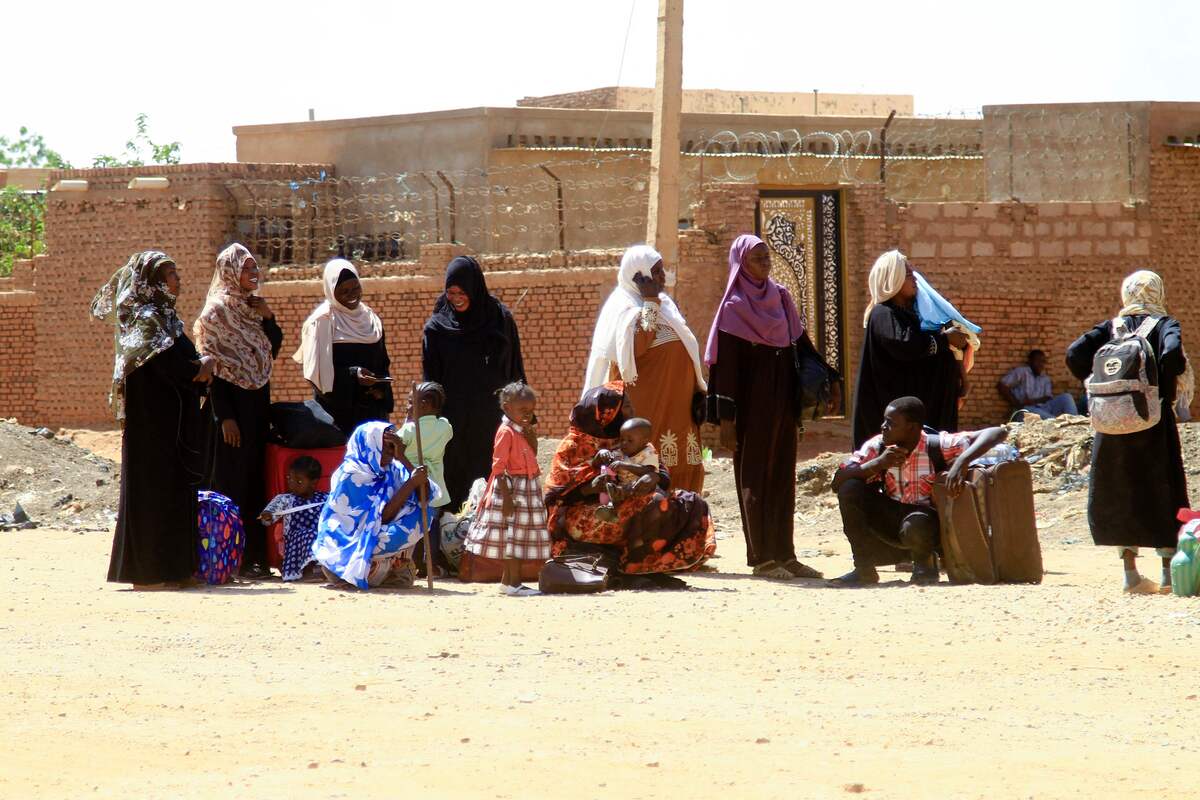 People fleeing street battles between the forces of two rival Sudanese generals, wait with their belongings along a road in the southern part of Khartoum, on April 21, 2023. Hundreds of people have been killed and thousands wounded since the fighting erupted on April 15 between forces loyal to Sudan's army chief and the commander of the powerful paramilitary Rapid Support Forces (RSF). (Photo by Ebrahim Hamid / AFP)