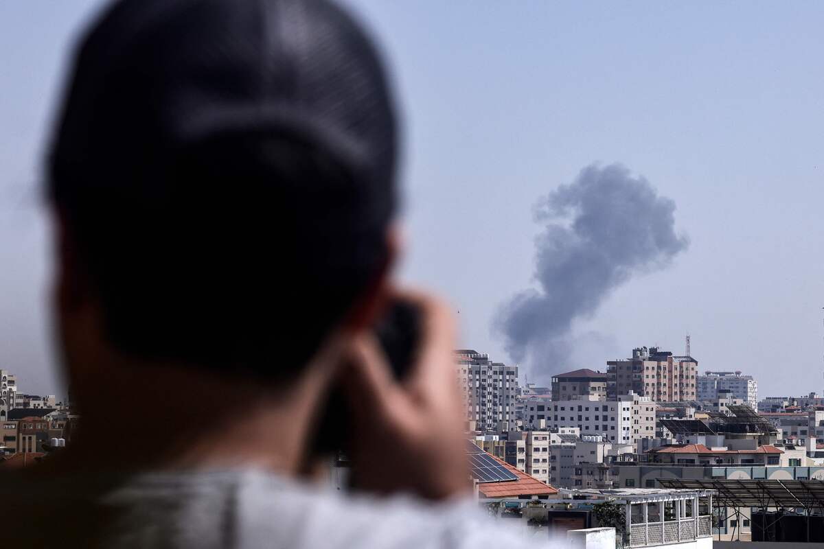 A man photographs smoke above buildings in Gaza City during an israeli air strike on May 11, 2023, on the third day of the worst escalation of violence in months that has killed 25 people in the blockaded Palestinian enclave. Air strikes by the Israeli army since May 9 have killed fighters as well as civilians, including several children, said officials in the crowded coastal territory. (Photo by MOHAMMED ABED / AFP)